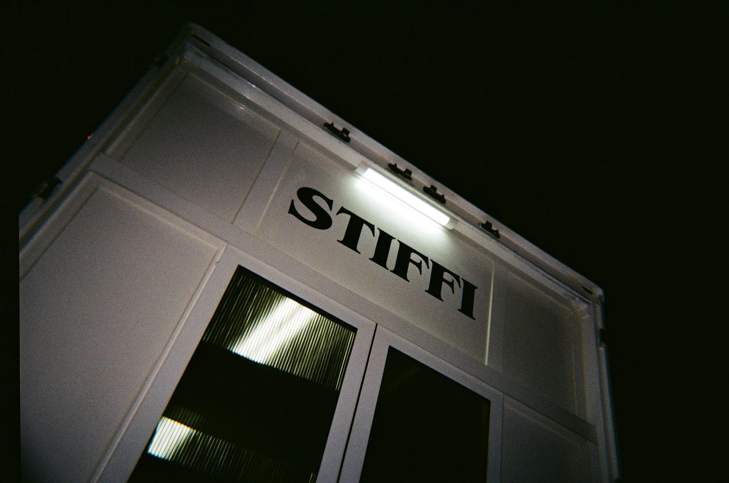 Esterno di una struttura bianca con la scritta 'STIFFI' illuminata, vista di lato contro un cielo scuro.