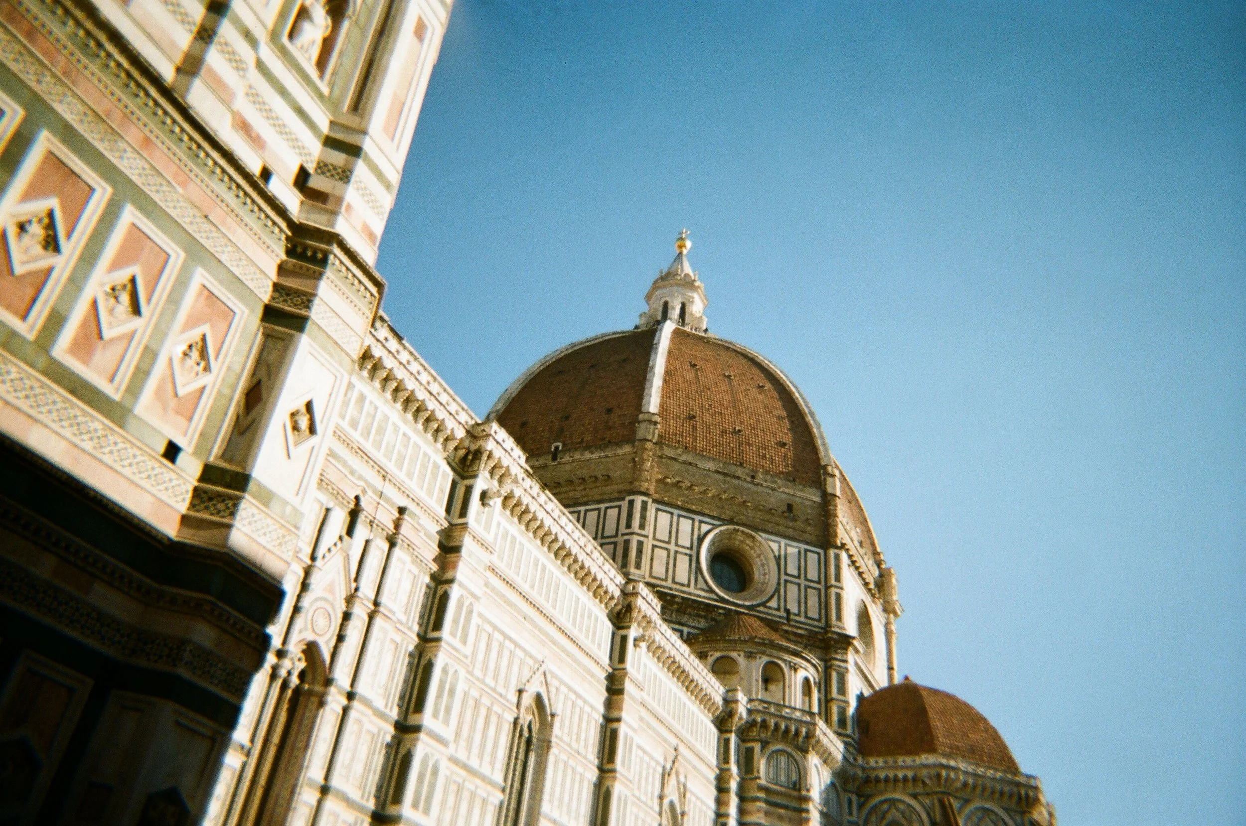 Vista della Cattedrale di Santa Maria del Fiore a Firenze con il suo grande cupolone in stile rinascimentale, in primo piano l'architettura decorativa della facciata e il cielo azzurro sullo sfondo.