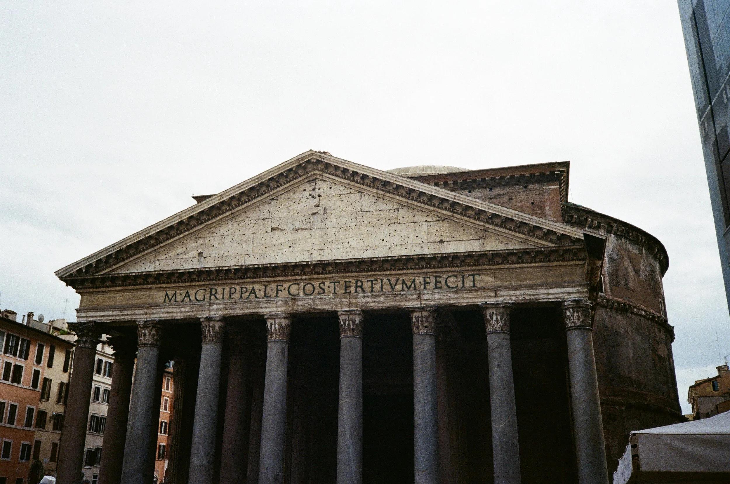 Il Pantheon di Roma con colonne e iscrizione latina sulla fronte, sotto un cielo nuvoloso.