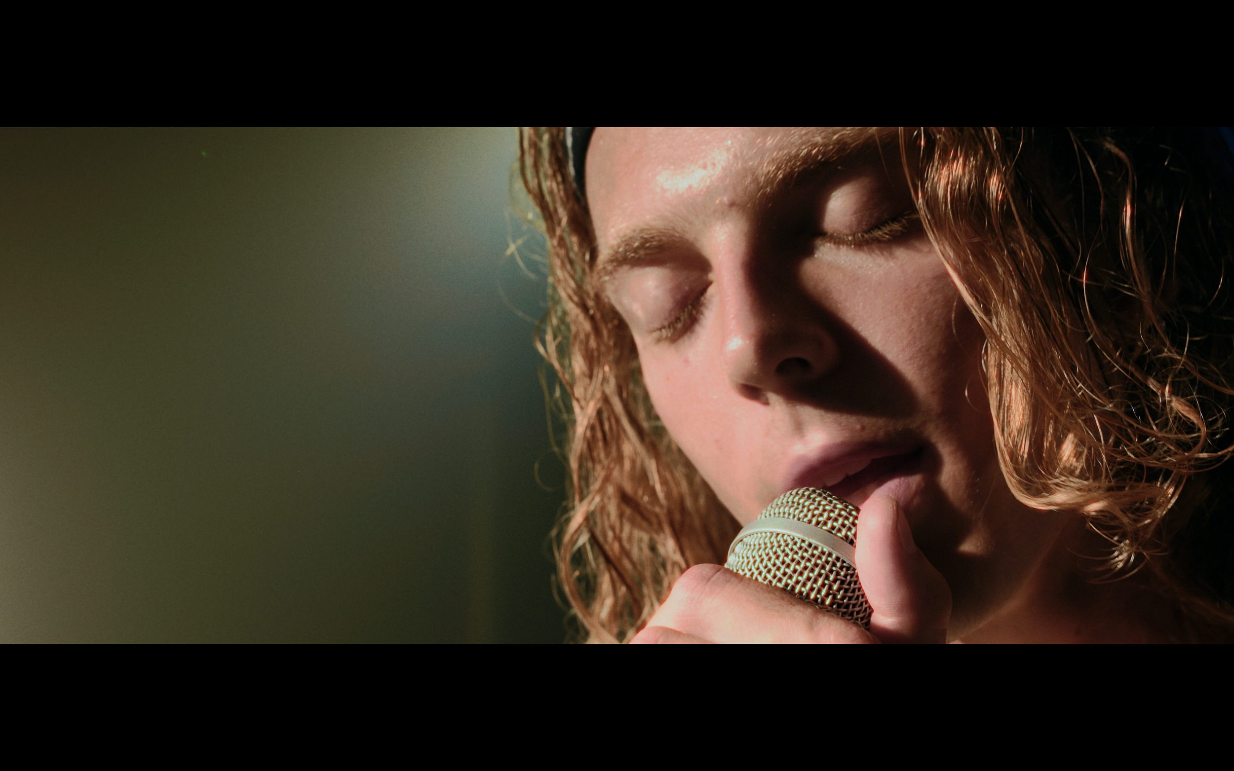 Una donna con capelli riccioli chiari tiene in mano un microfono mentre canta con gli occhi chiusi