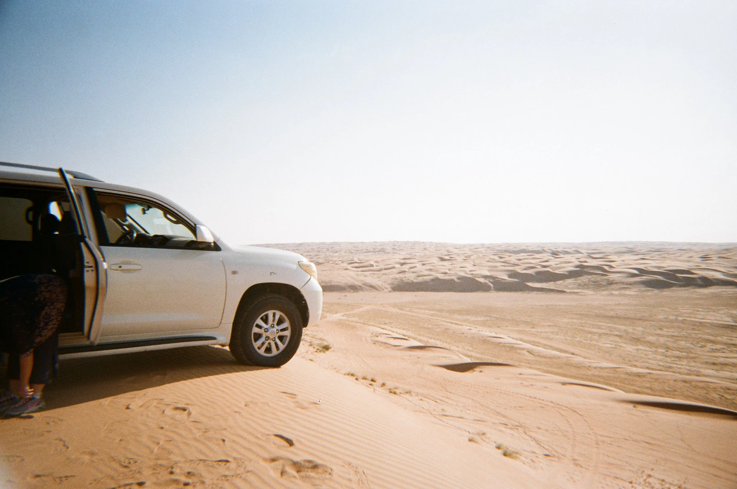 Auto in un deserto di sabbia con una persona accovacciata vicino alla porta aperta