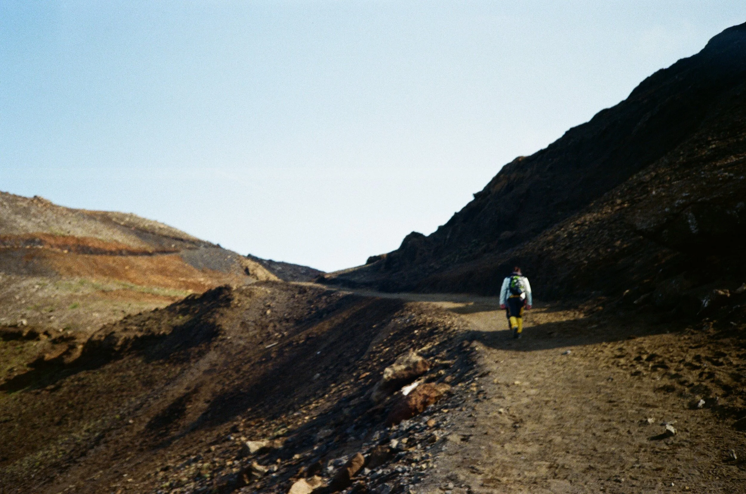 Escursionista che cammina lungo un sentiero montano in un paesaggio arido e roccioso.