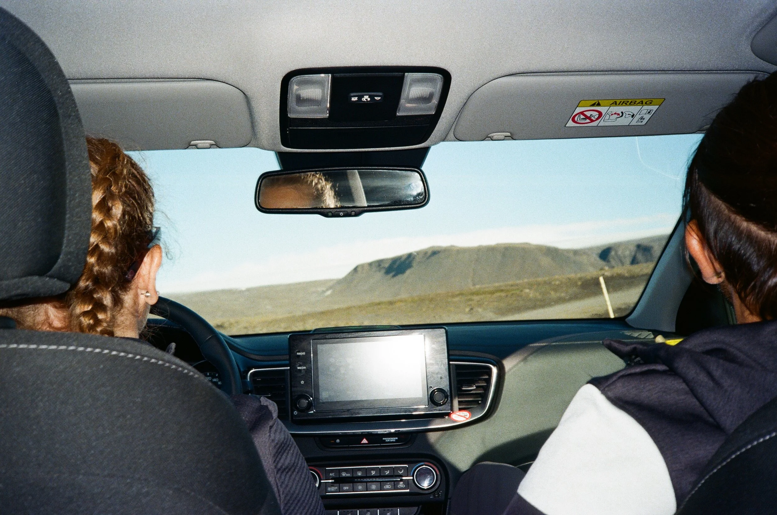 Interno di un'auto vista dall'interno con due passeggeri, uno dei quali vede il panorama di un paesaggio montano attraverso il parabrezza.