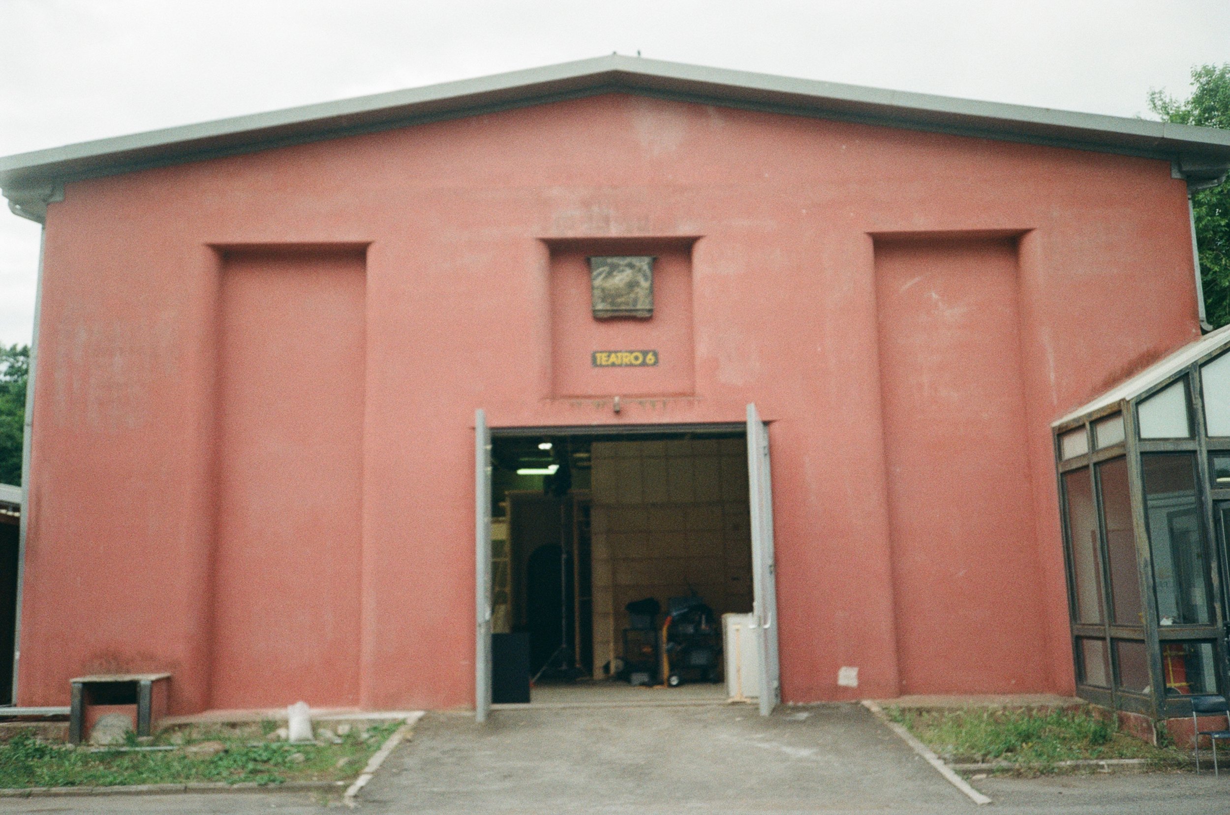 Facciata di un teatro con ingresso aperto, pareti di colore rosso, e un cartello con scritto 'TEATRO 6' sopra l'ingresso.