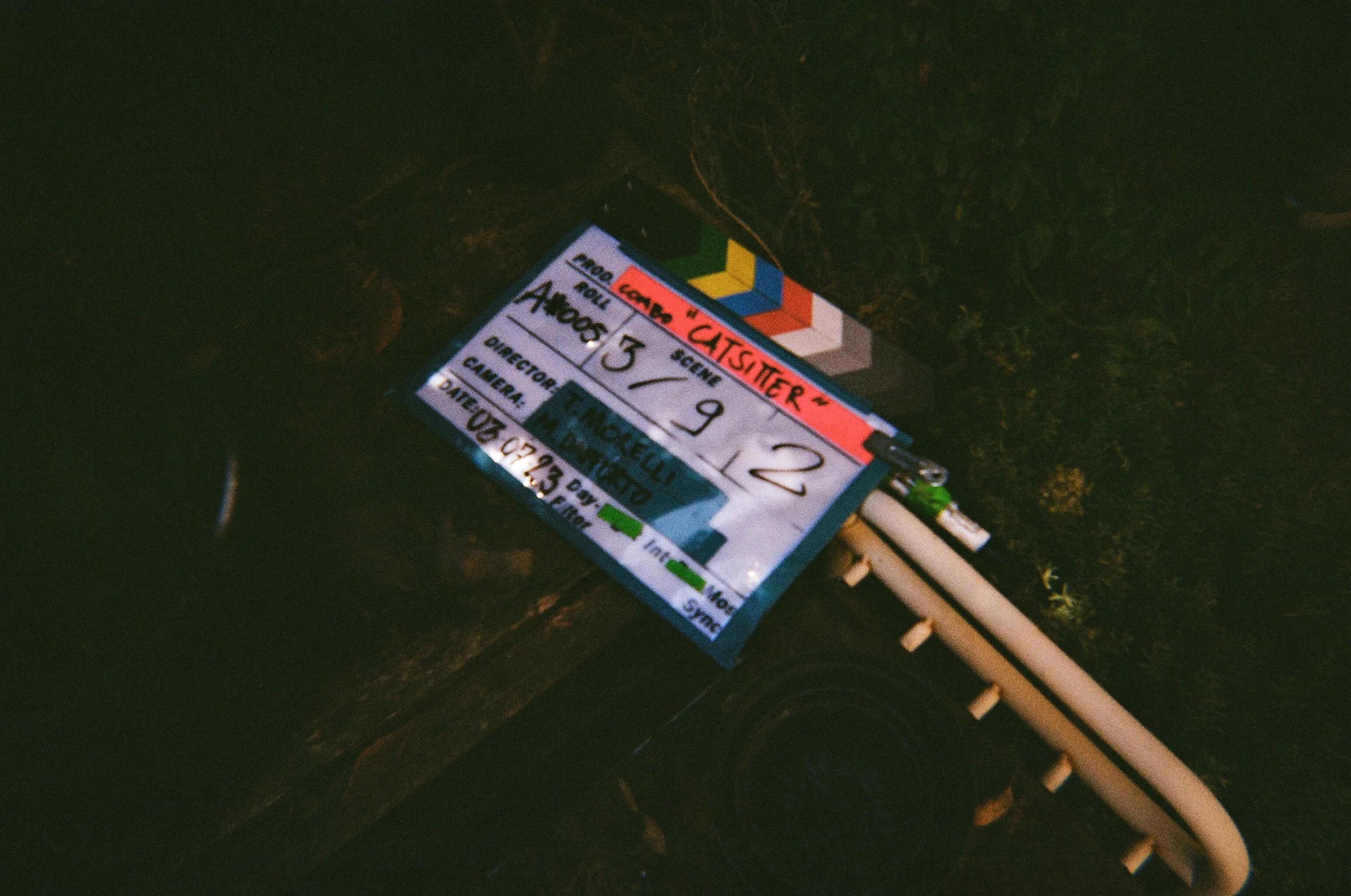 Tabellone indicante un set di uno spettacolo teatrale con dettagli sull'autore, regista e data, illuminato in ambientazione scura con luci soffuse.