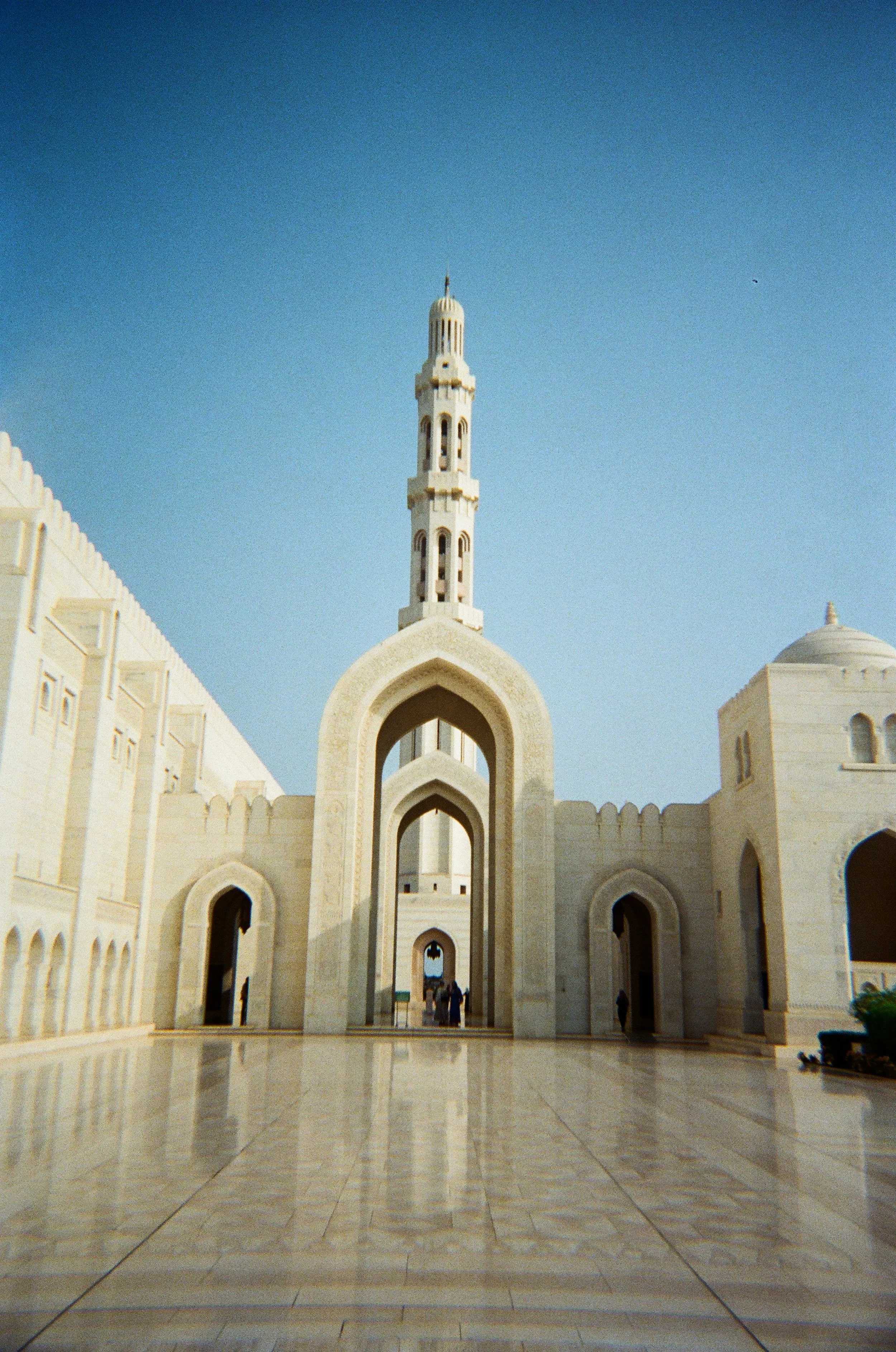 Un edificio religioso con archi, una torre alta e un soffitto decorato, in un luogo pubblico con pavimento di marmo e alcune persone in lontananza.