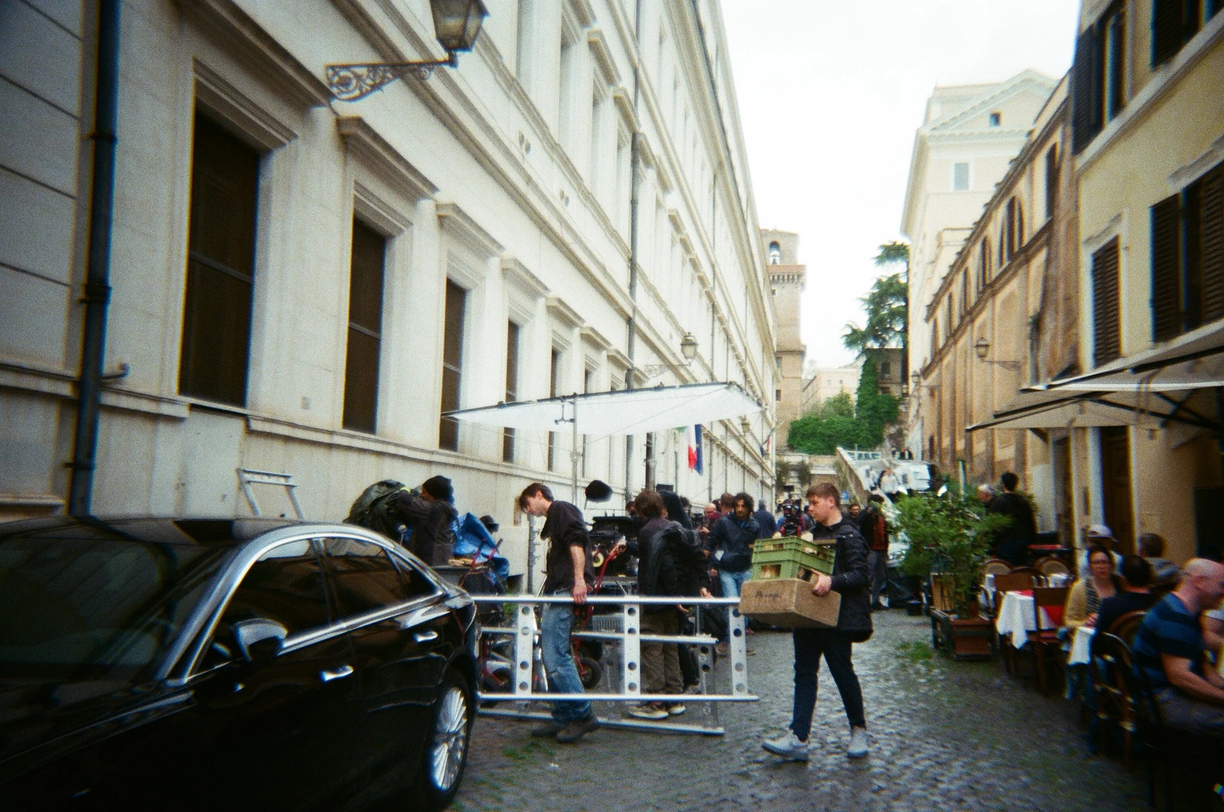 Persone che lavorano e mangiano in un ristorante all'aperto su una strada di ciottoli tra vecchi edifici