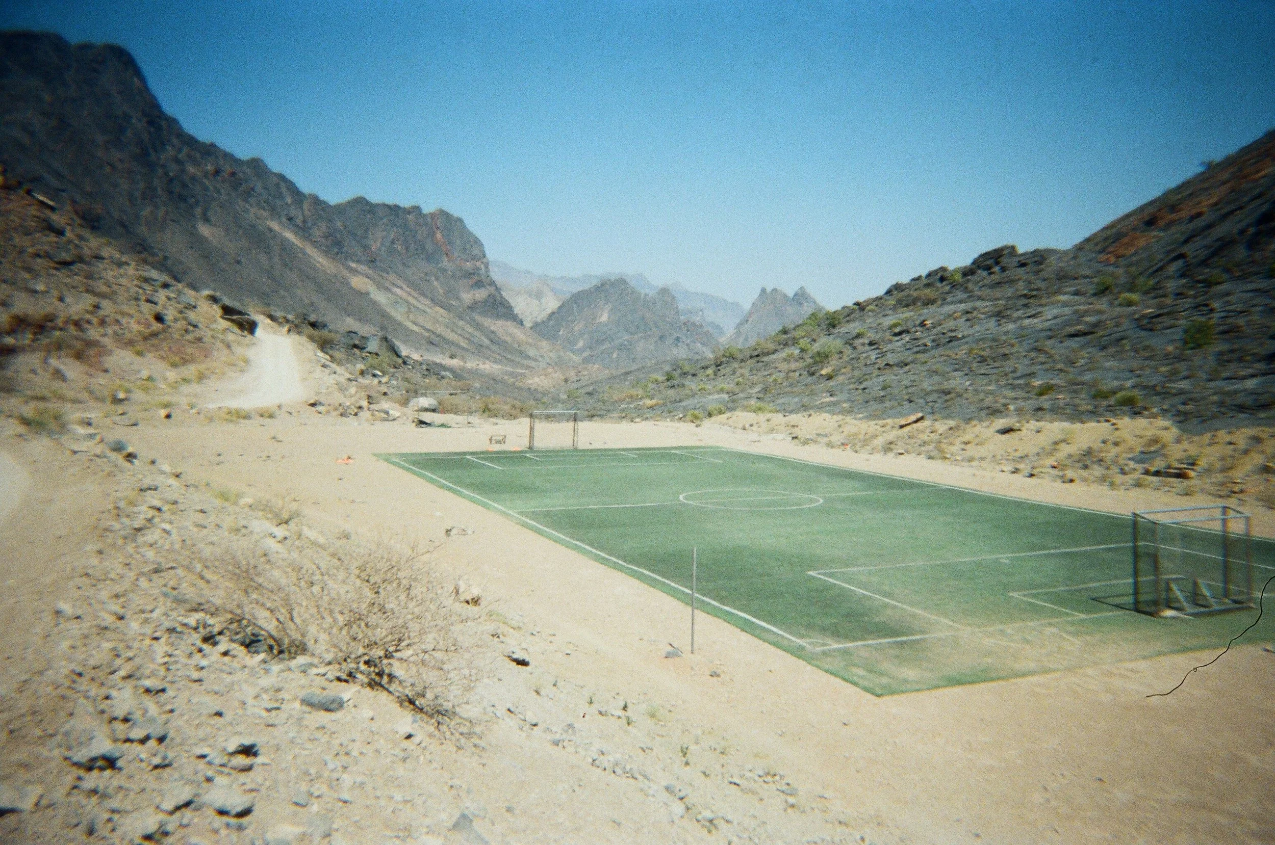 Campo da calcio abbandonato in un paesaggio desertico montano con montagne in lontananza e cielo azzurro