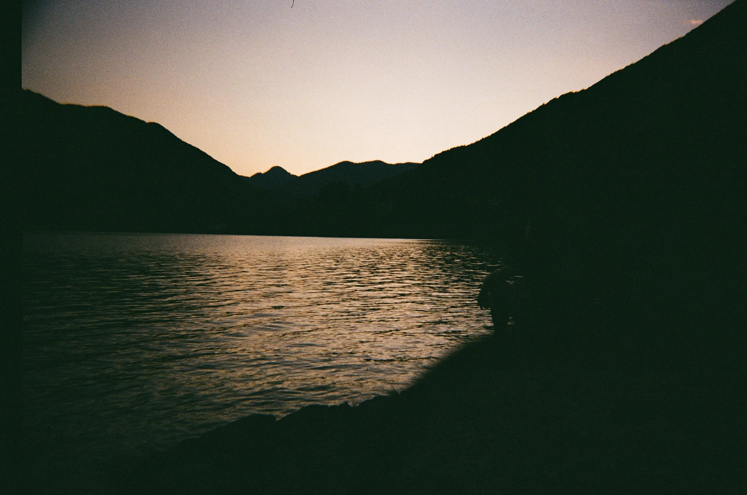 Paesaggio al tramonto con montagne scure che si riflettono in un lago calmo