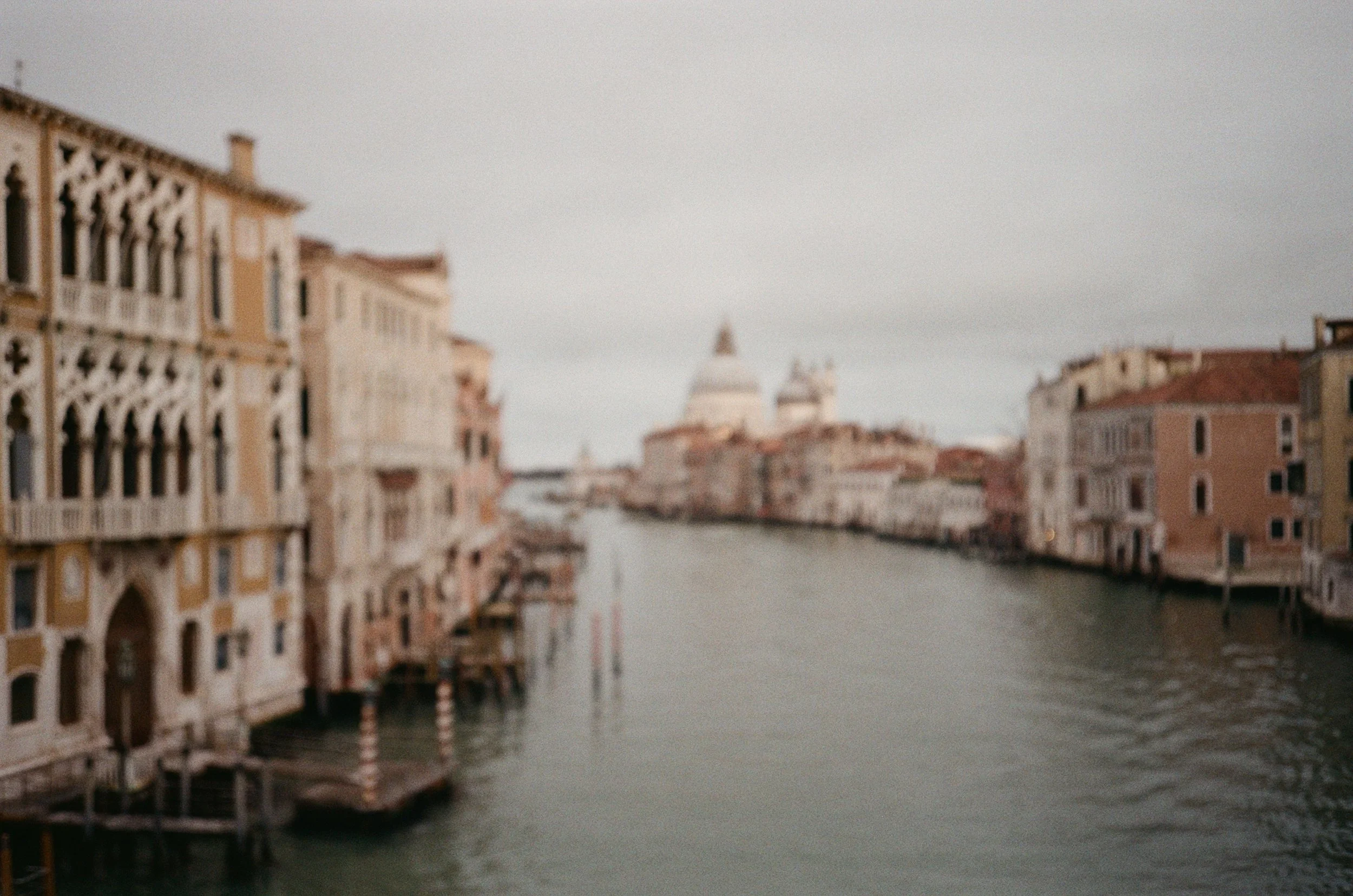 Immagine sfocata di un canale in Venezia con edifici storici ai lati e la Basilica di Santa Maria della Salute in lontananza.