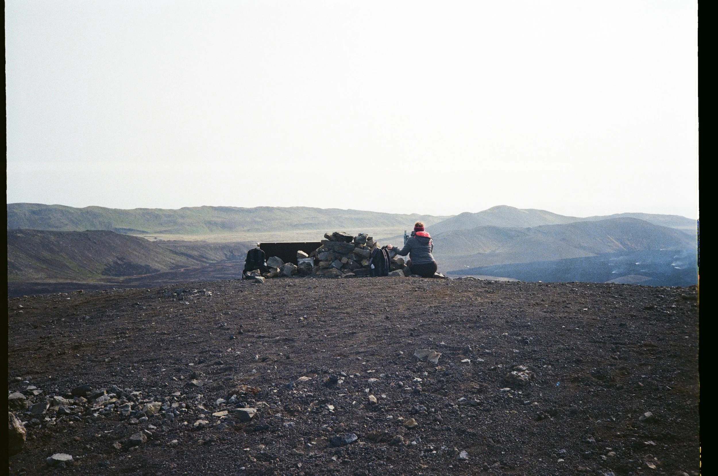 Persona seduta su una roccia in un paesaggio montano, con sacchetti e un tavolo di pietra