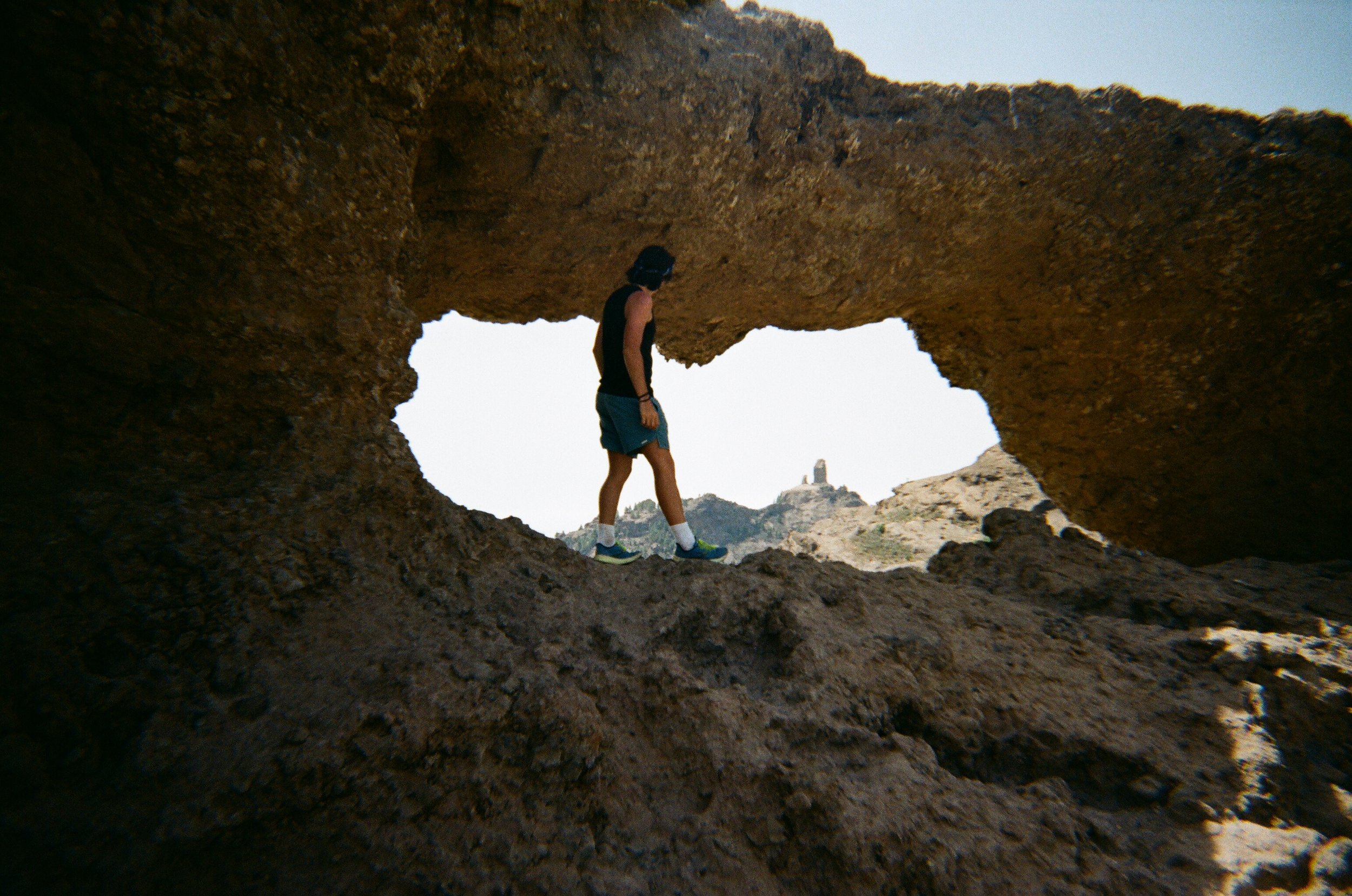 Persona che cammina attraverso una formazione rocciosa con un'apertura che ricorda una finestra naturale, con una roccia in lontananza su una collina.