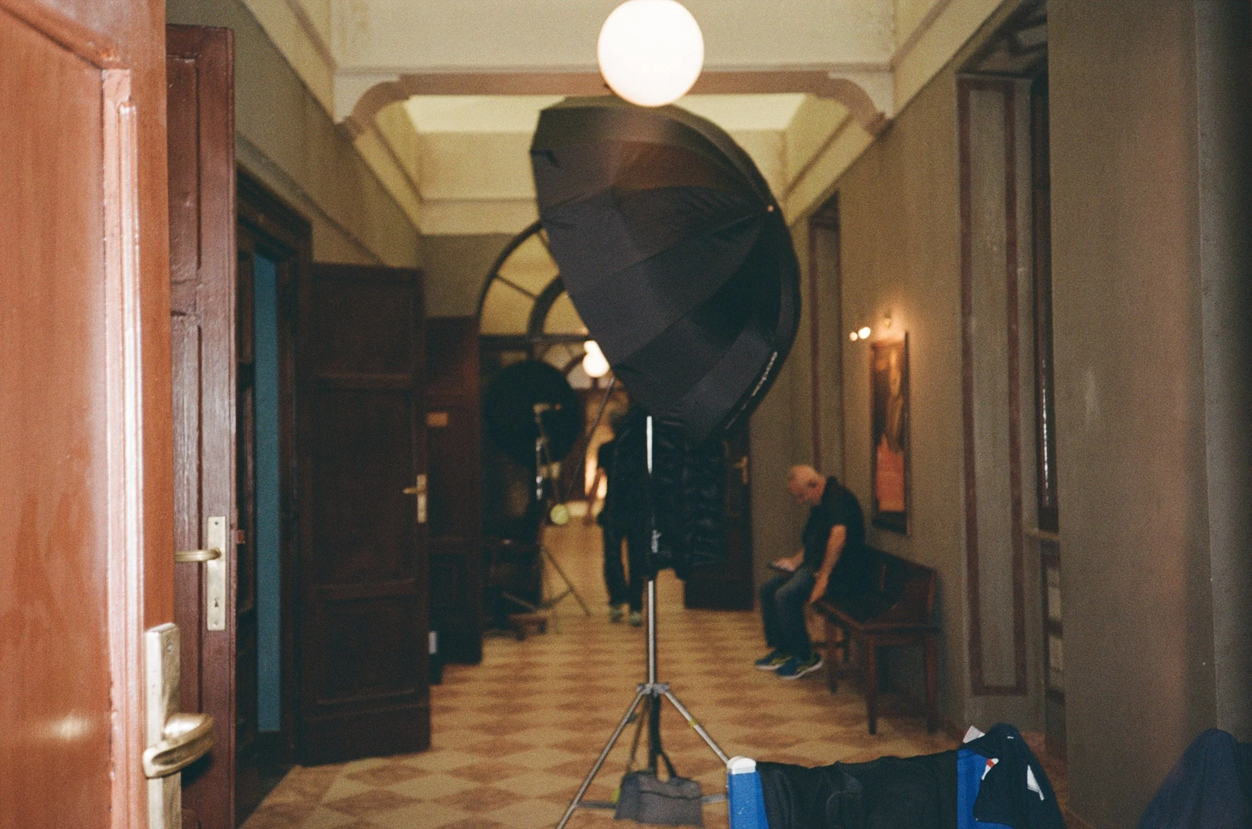 Interno con luci soffuse, sedie di legno e un set di luci e ombrelloni fotografici per riprese. Persone sedute e attrezzature fotografiche.