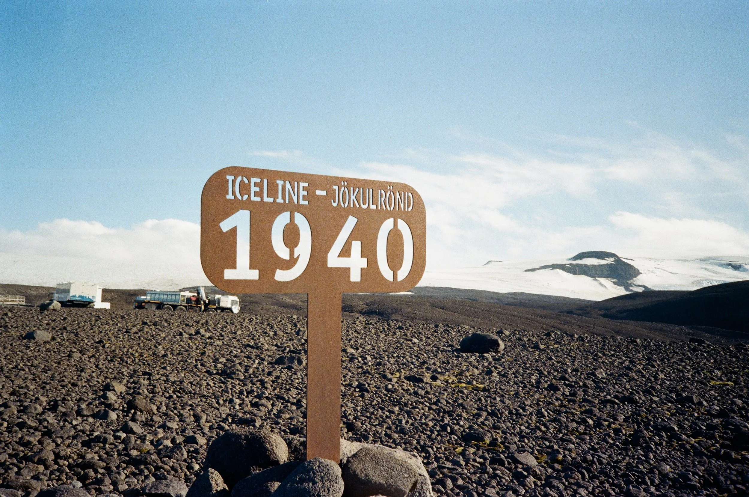 Segnale stradale con scritta 'Iceland - Jökulrönd 1940' su paesaggio di lava e ghiacciaio lontano.