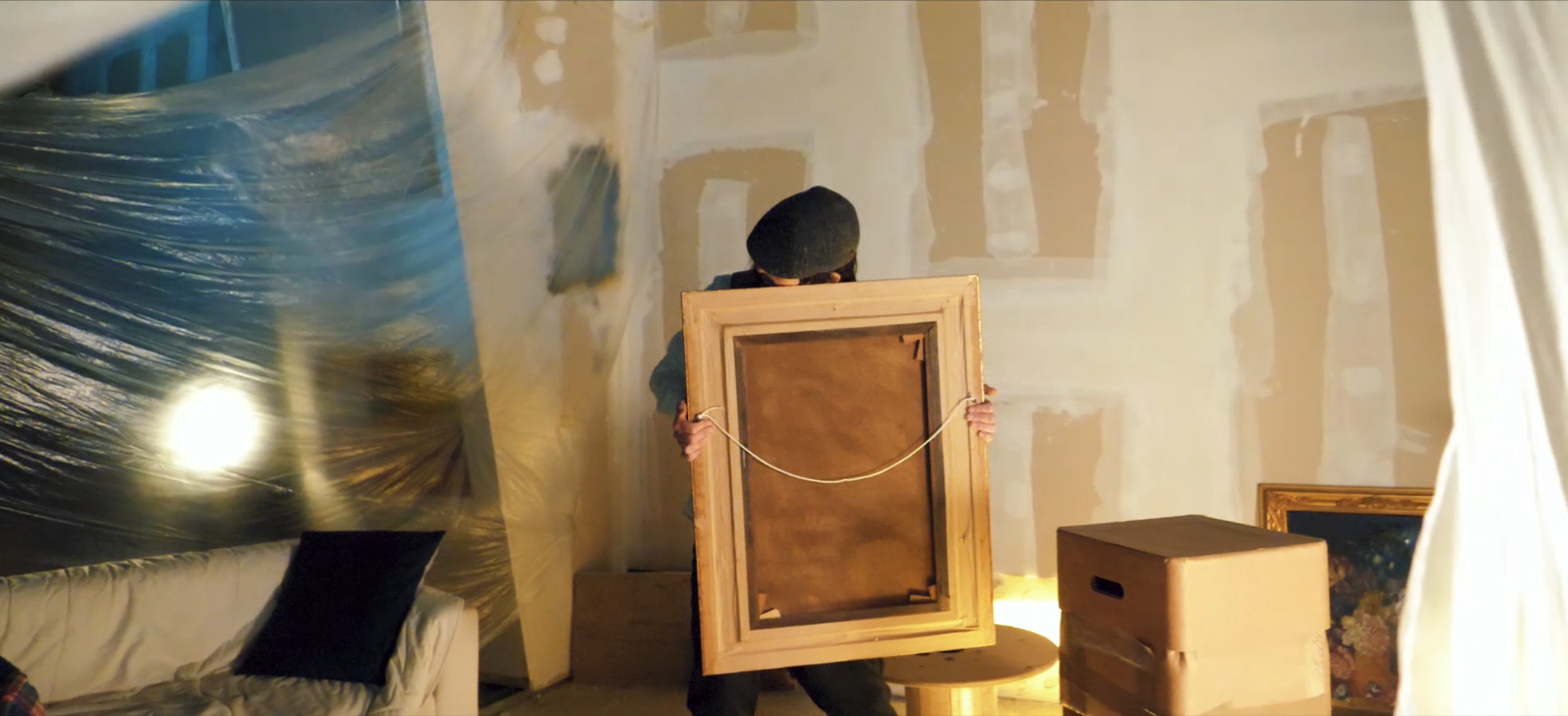 Persona che tiene un quadro rotondo di grandi dimensioni in una stanza con pareti non finite e decorazioni artistiche.