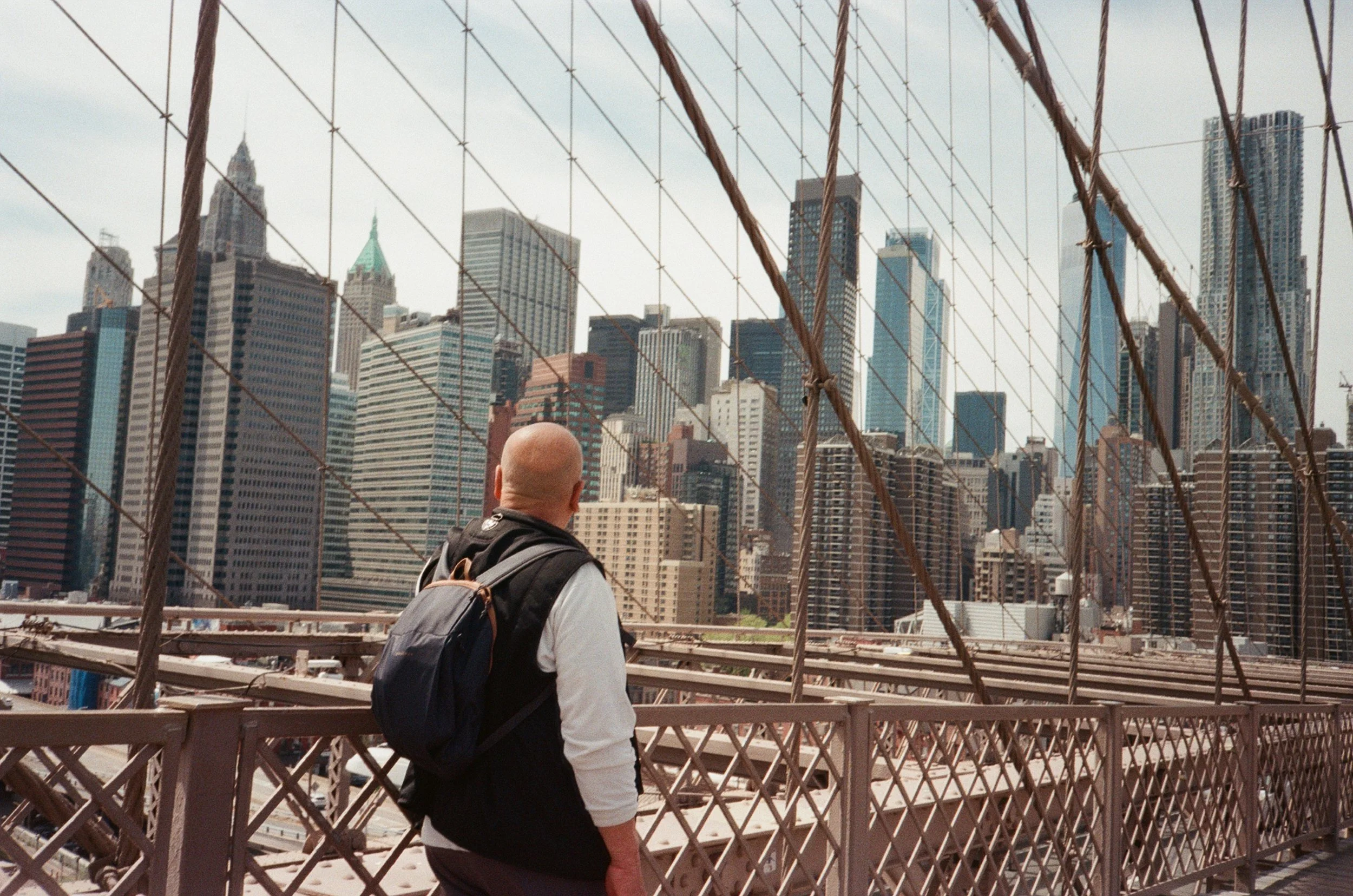 Persona con zaino che guarda lo skyline di Manhattan attraverso la ringhiera del Brooklyn Bridge.