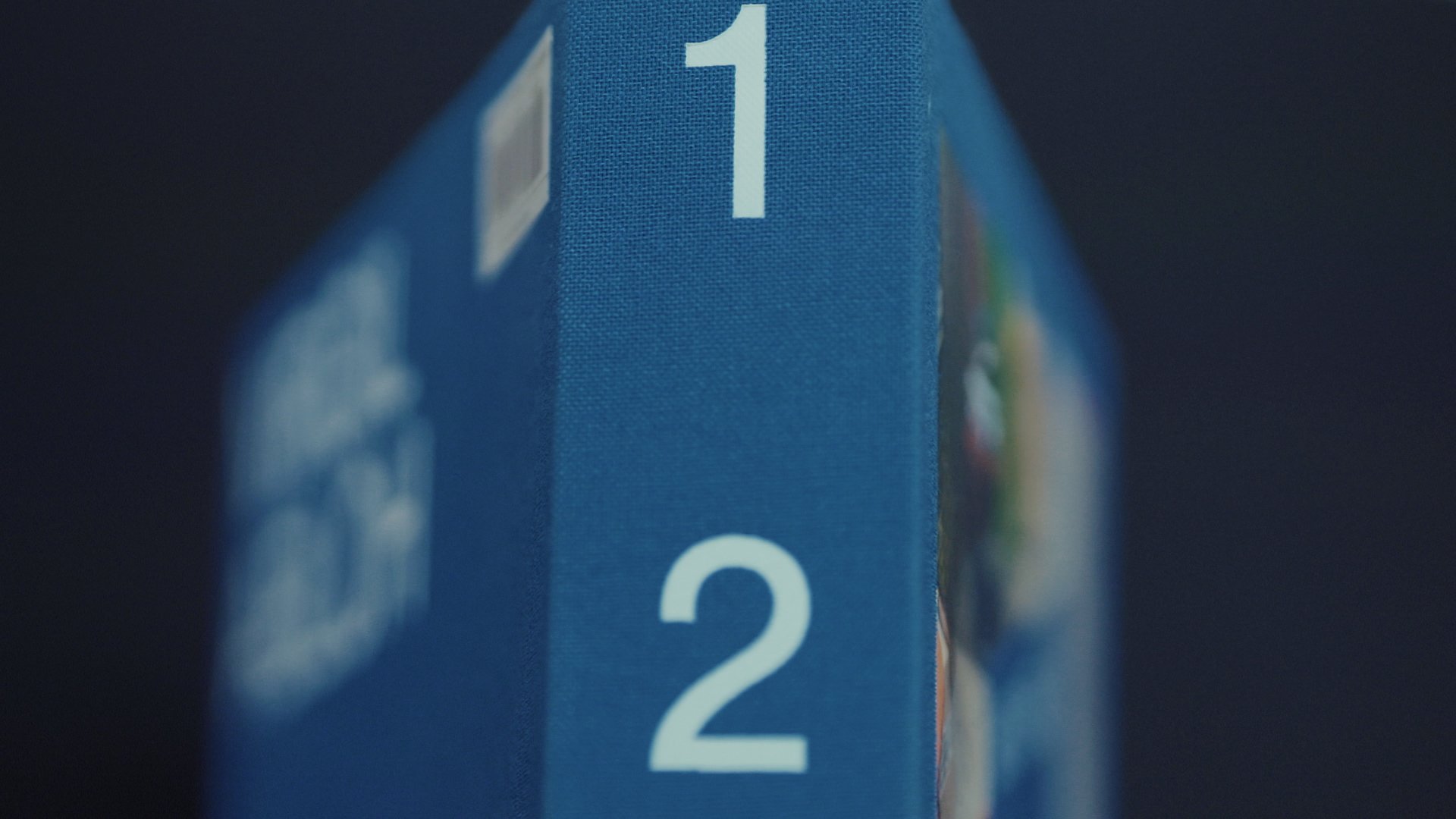 Dettaglio laterale di una scatola blu con numeri 1 e 2 evidenziati, sfondo nero.