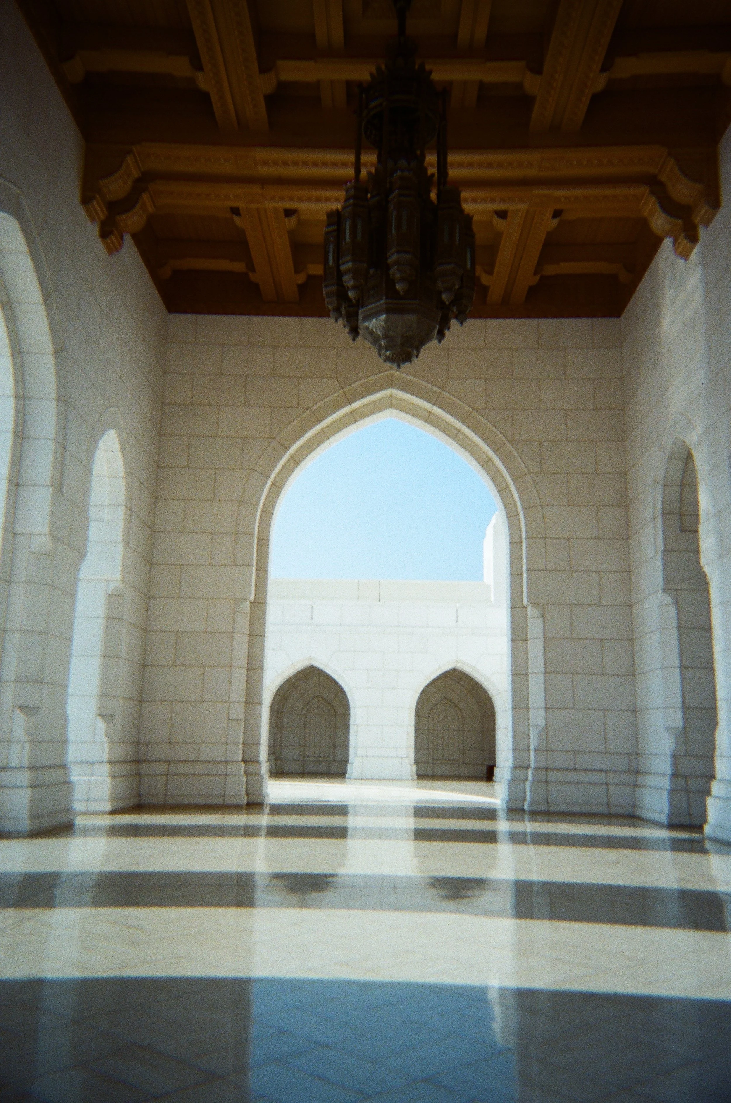 Interno di una moschea con archi, pareti in pietra chiara e un grande lampadario di legno e metallo appeso dal soffitto in legno.