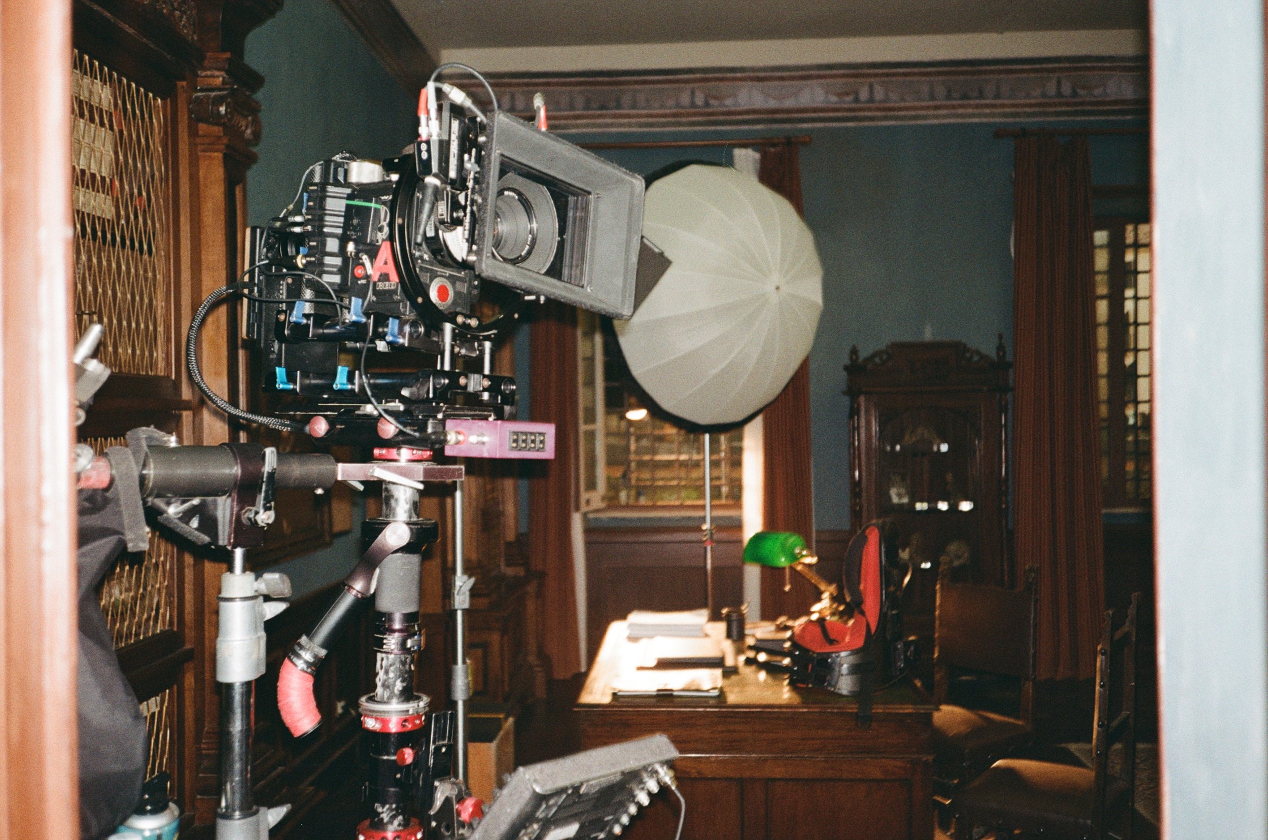 Interno di uno studio con attrezzature cinematografiche, tra cui una telecamera grande e un ombrello per la luce, su un tavolo con vari oggetti e mobili di legno.