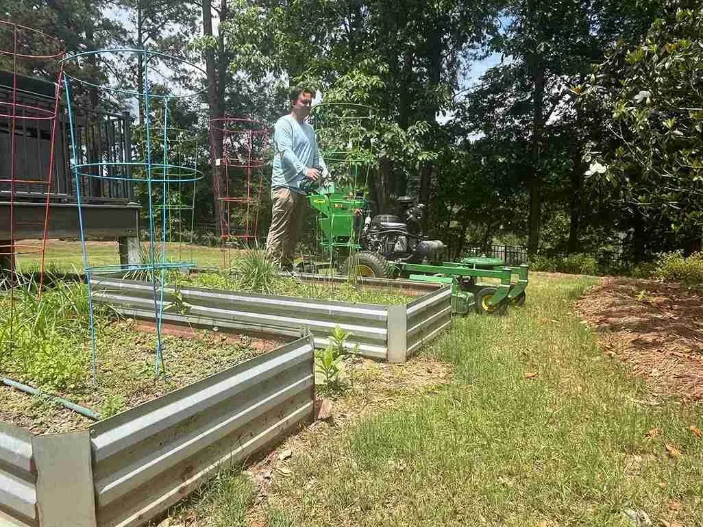 Mowing grass with green John Deere mower near vegetable garden