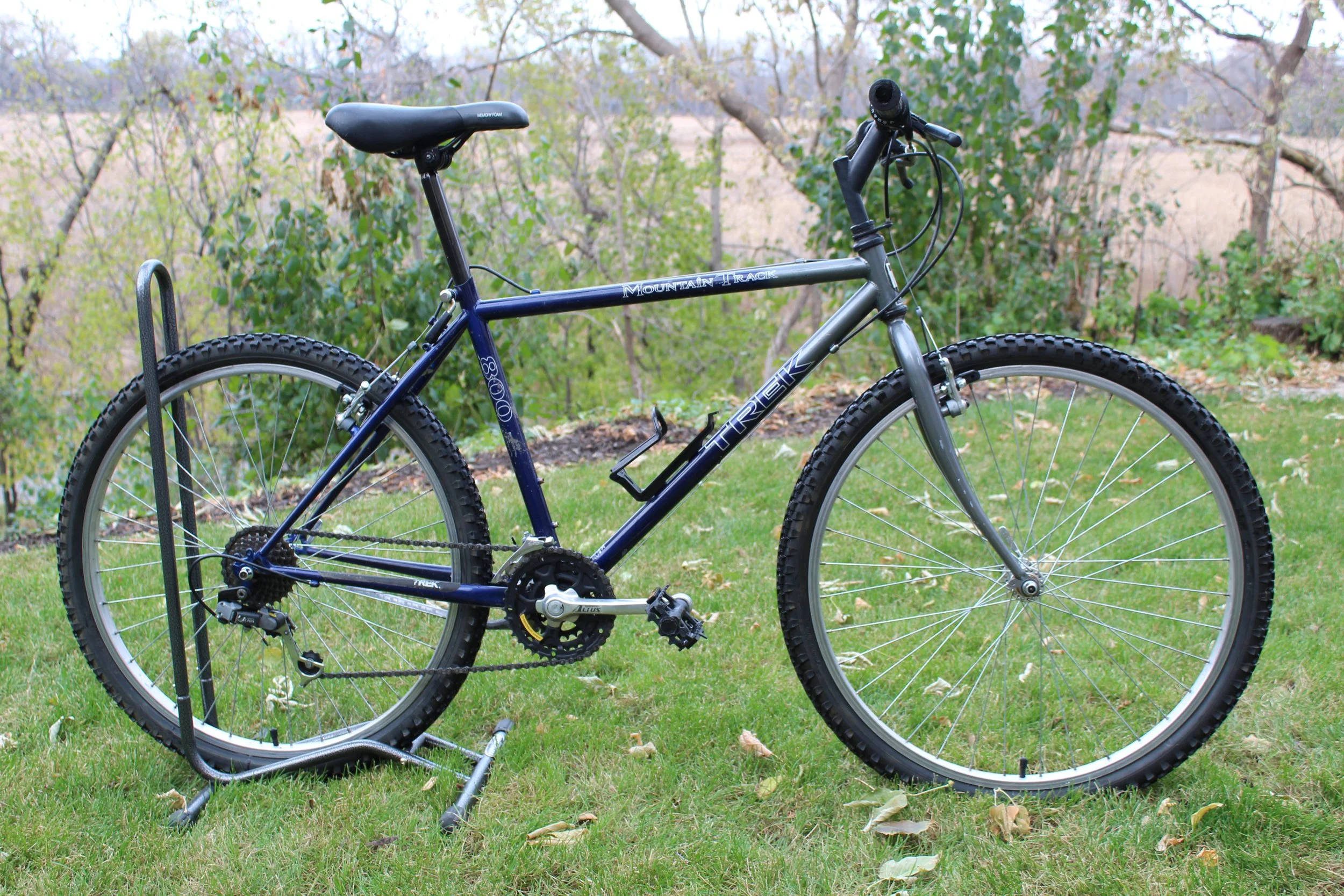 A Trek 8000 mountain bike with a blue frame and black seat parked on grass with a backdrop of trees.