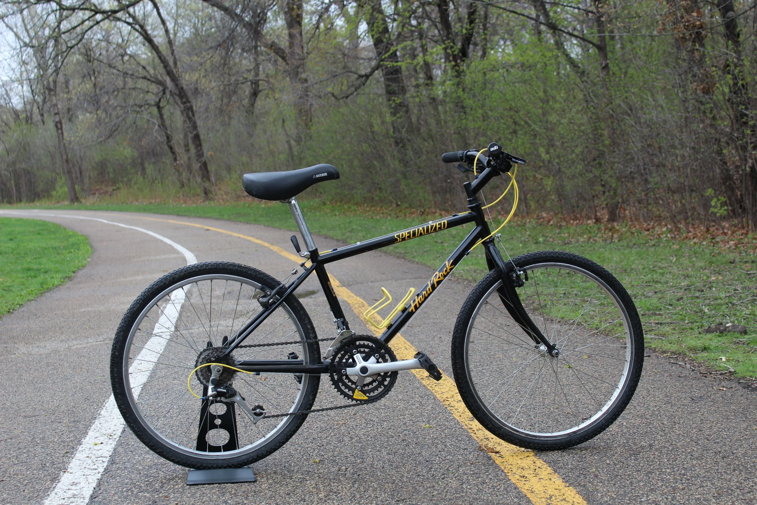 Black and yellow mountain bike on a paved trail in a wooded area.