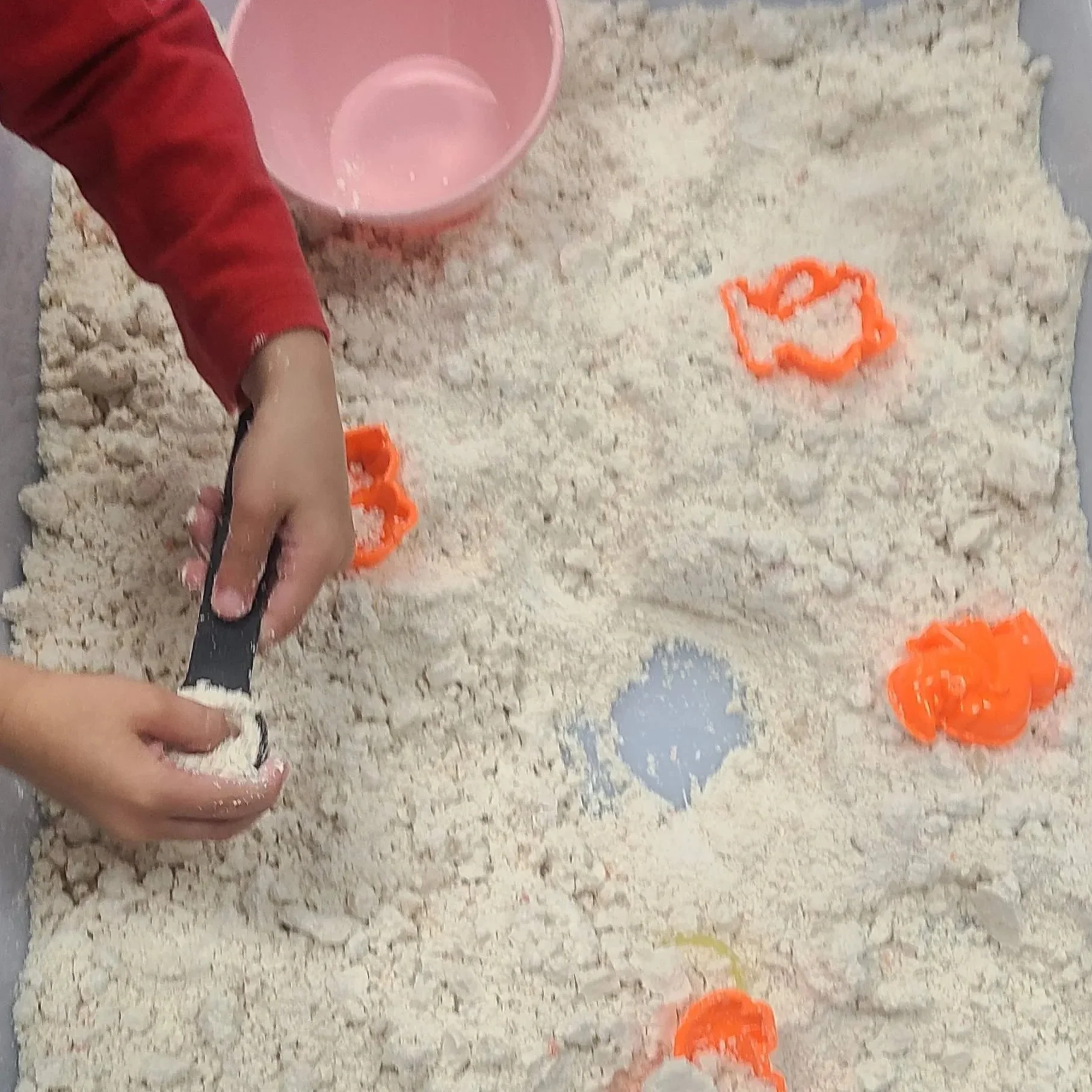 Preschool child pressing playdough molds into a mixture of flour and oil to create crumbling fossil impressions during a sensory STEAM activity.