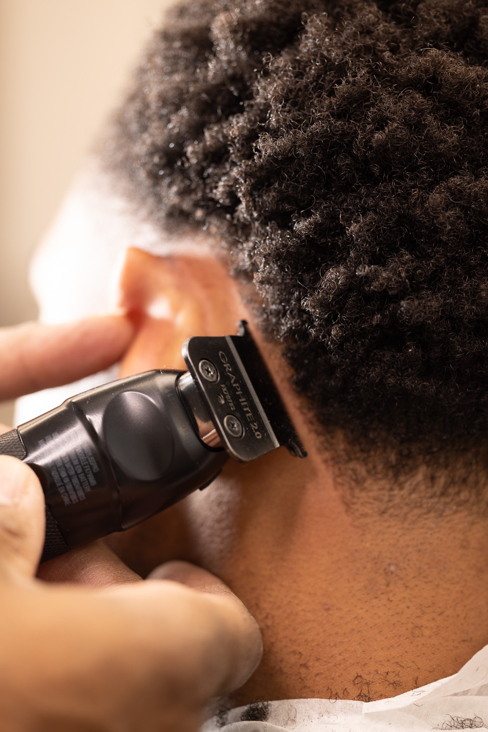 A person getting an ear hair trim with an electric trimmer in a barbershop or salon setting.