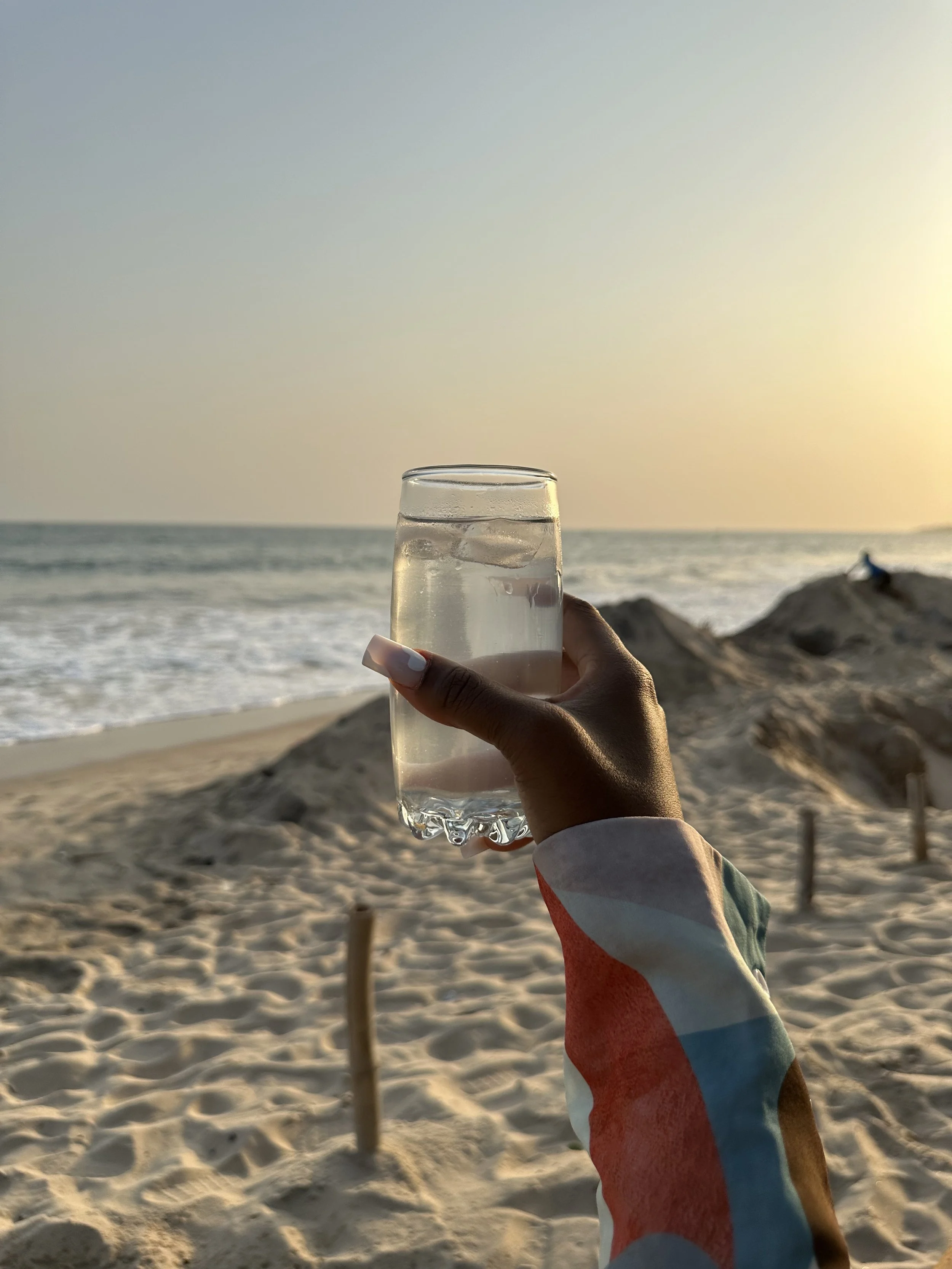 Woman holding a water glass while sitting on the beach representing starting a micro-habit of drinking a glass of water every morning