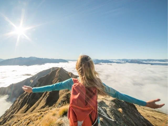 a woman standing on a mountain peak above the clouds after balancing life
