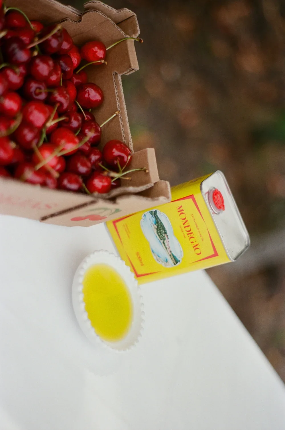A carton of fresh red cherries, a small dish of cherry juice, and a can of Oregon hazelnut syrup on a white surface.