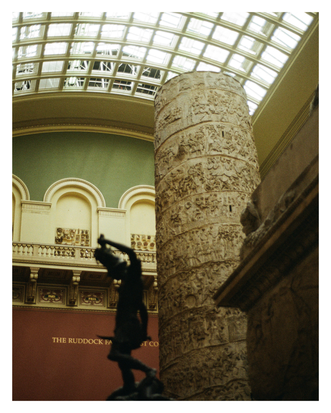 Ancient stone column with intricate carvings inside a museum with a glass ceiling.