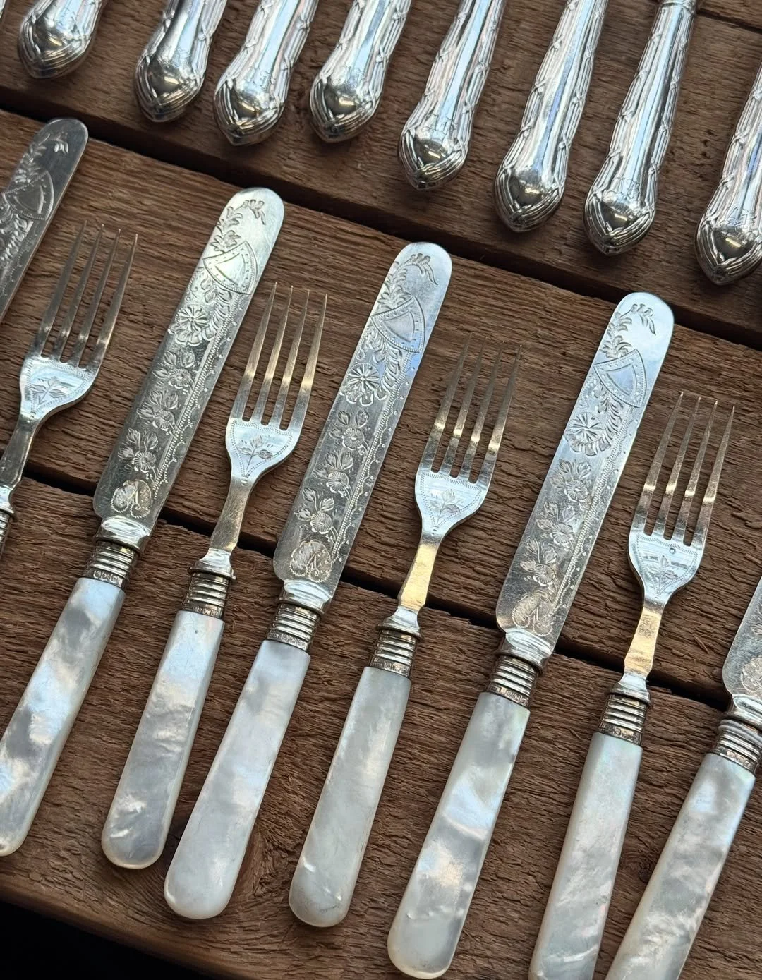 Set of vintage silverware with engraved floral and shield designs, including knives and forks, arranged on a wooden surface.