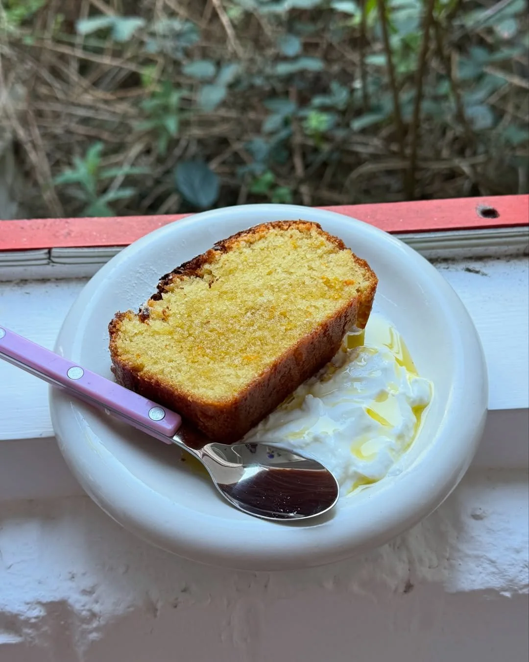 Slice of lemon pound cake with whipped cream and a drizzle of honey on a white plate.