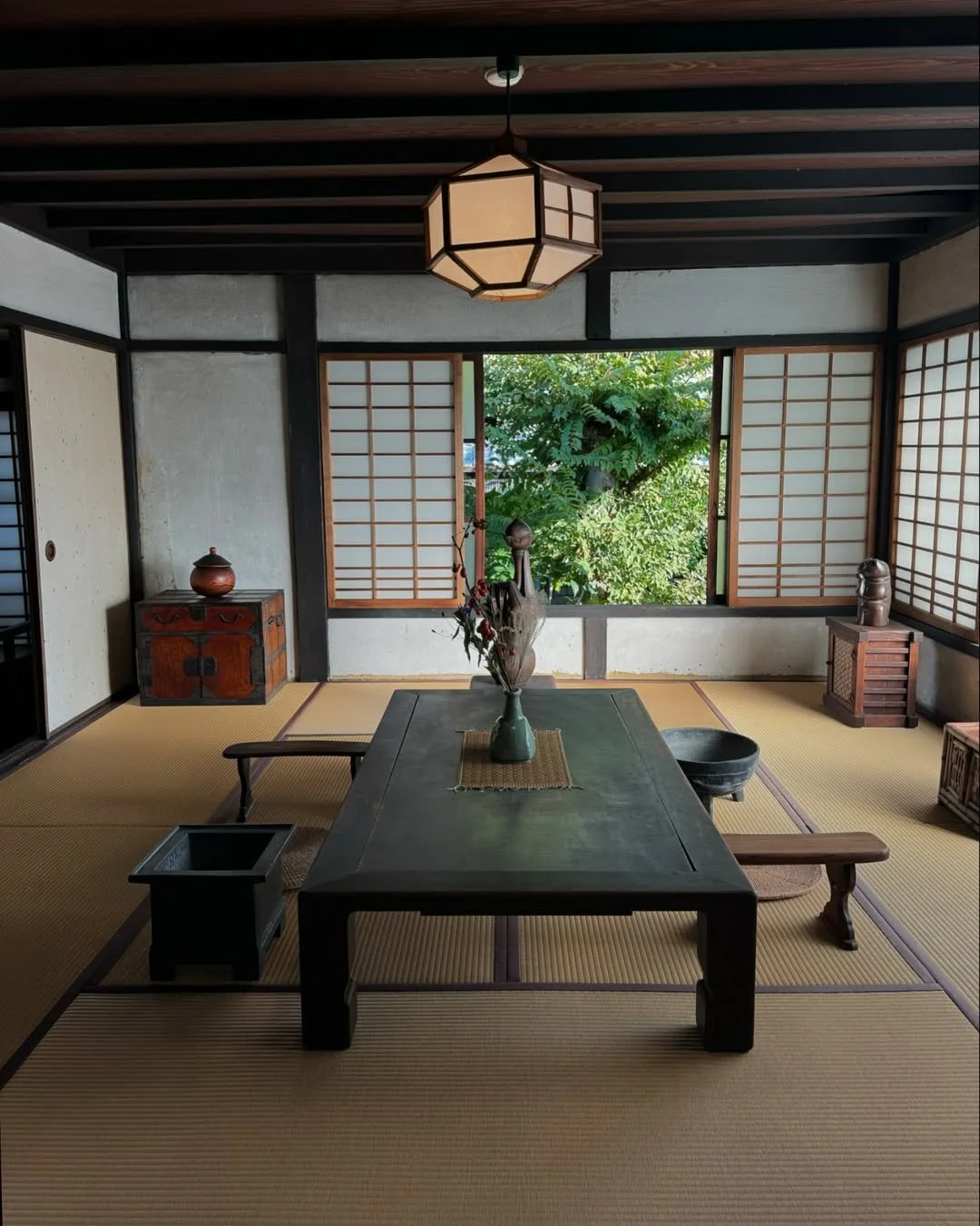 Traditional Japanese room with tatami mats, low wooden table, shoji screens, and greenery outside the window.