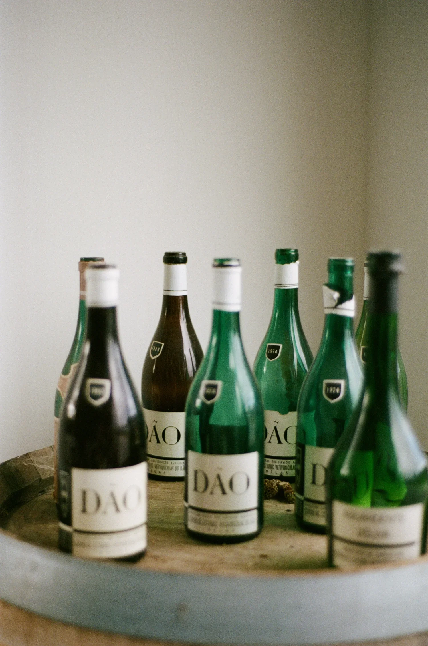 Several green and dark glass wine bottles with white labels on a round wooden tray.