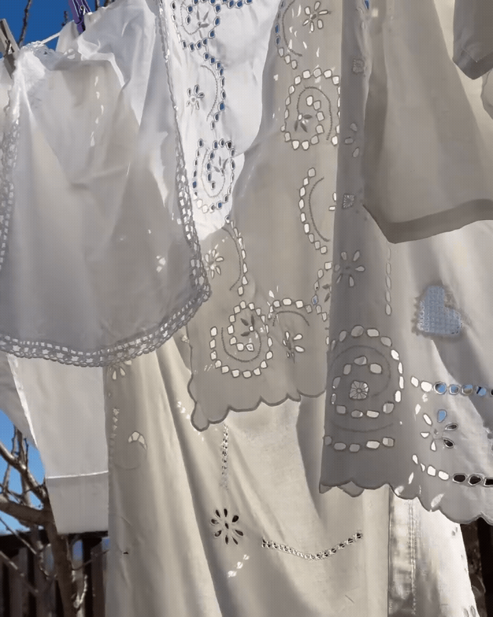 Close-up of white embroidered fabric hanging outdoors, with a clear blue sky in the background.
