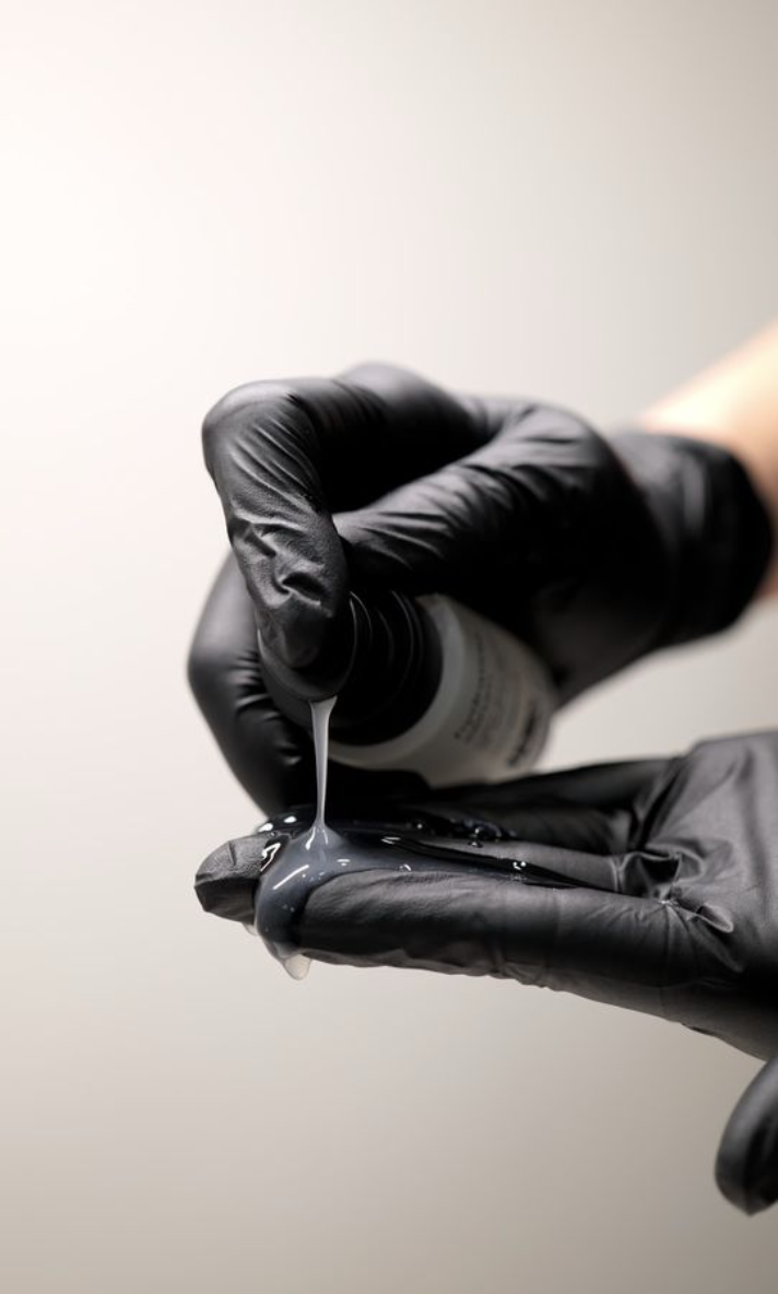 A hand wearing a black glove pouring clear liquid from a small bottle.