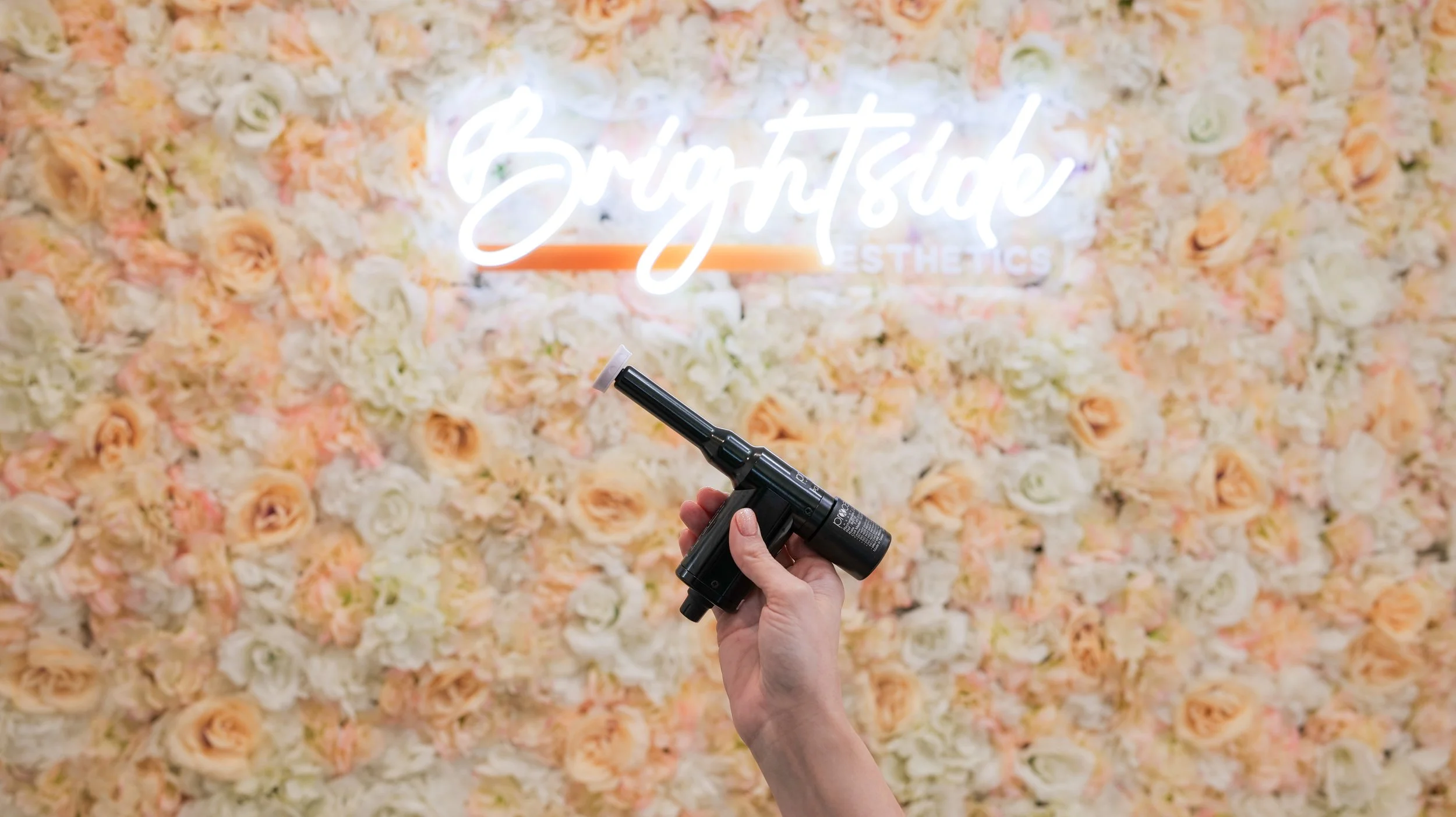 A hand holding a small blow torch over a background of cream, peach, and white roses with a neon sign that says "Beauty Studio".