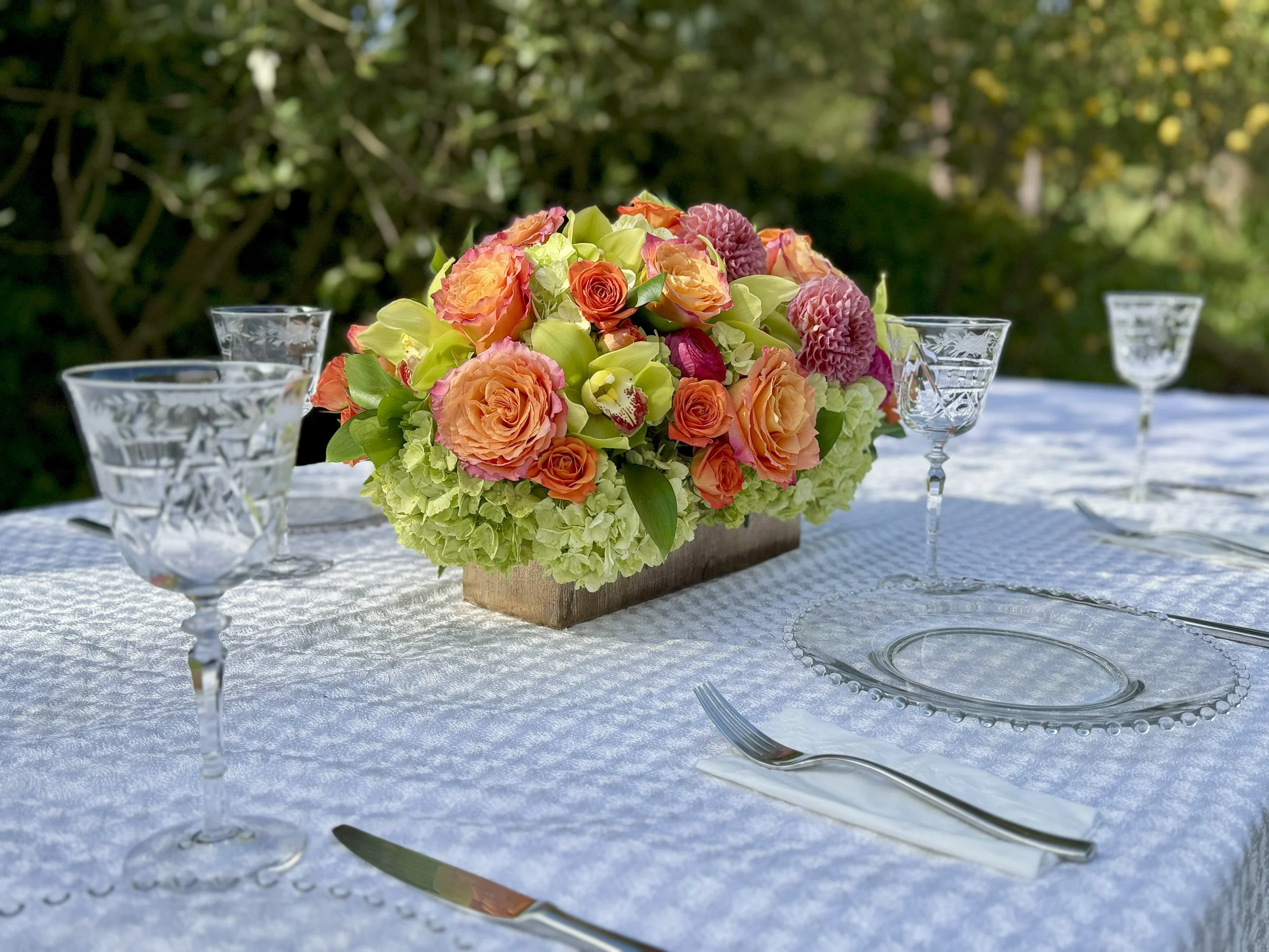 Candlewick glass plate with a beaded rim beside etched cut-crystal goblets and a floral centerpiece on a damask cloth, an outdoor table setting