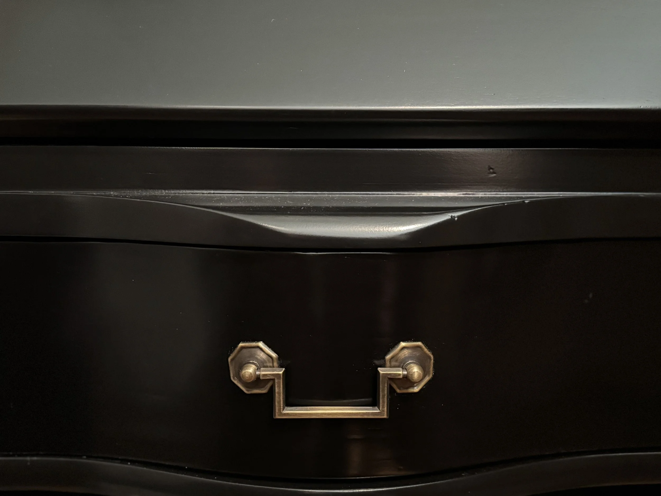 Detail of a serpentine drawer front and its Chippendale rosette pull in hand-finished brass on the black-lacquered case