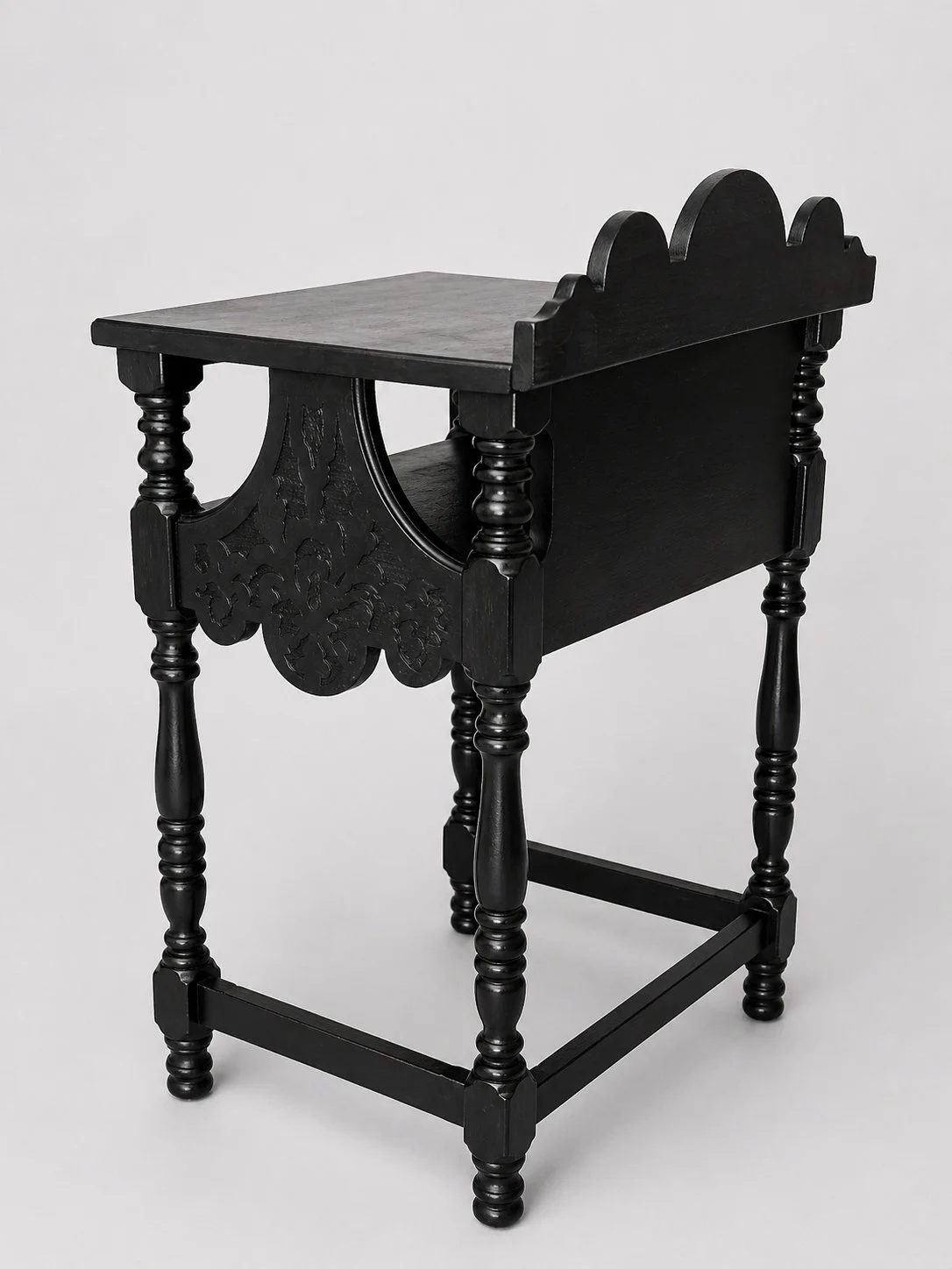 Angled view of black refinished telephone stand showing curved apron cutout, turned legs, and lower tier