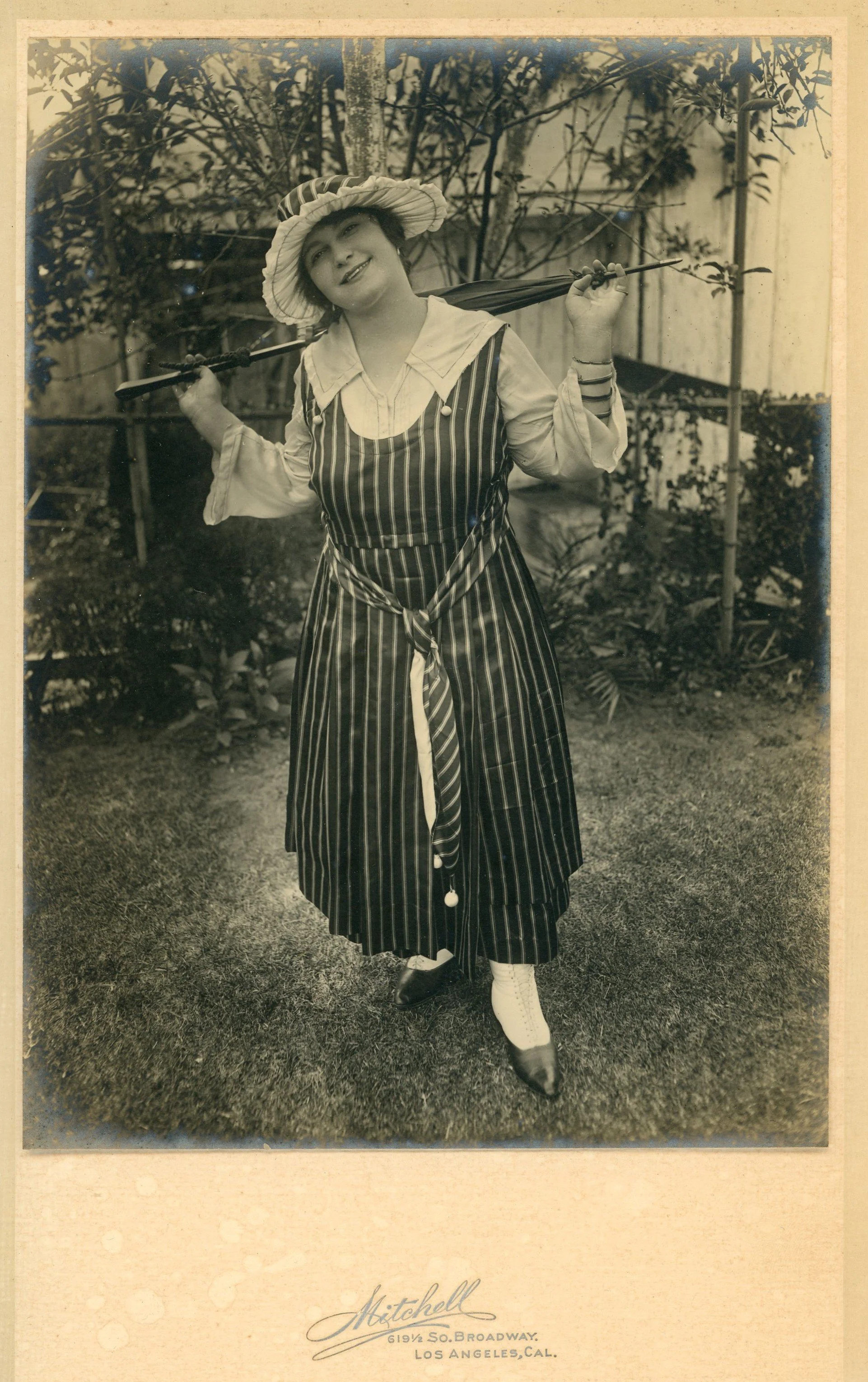 Studio portrait of a young woman in a striped dress with a parasol, Los Angeles, about 1918.