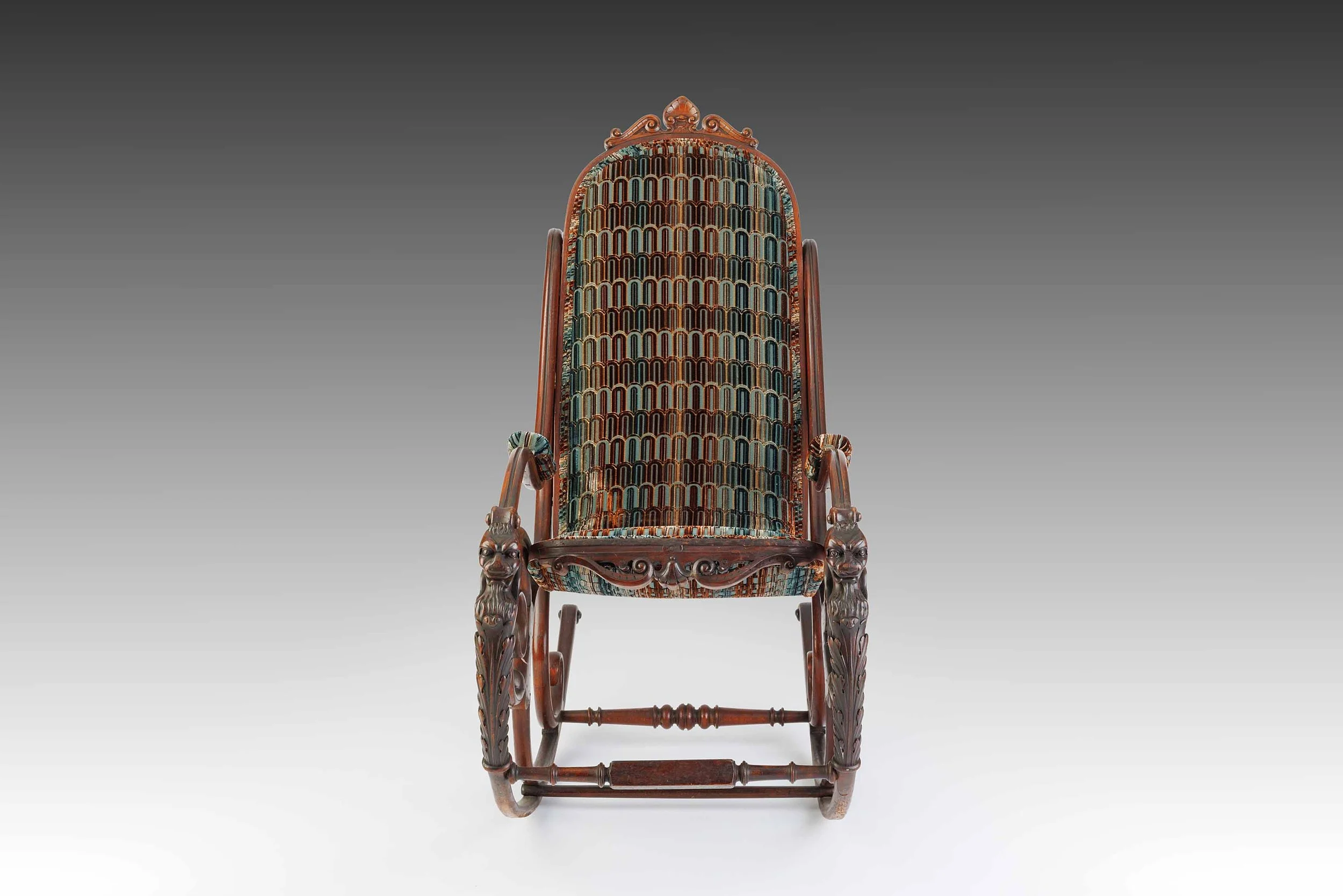 Frontal view of The Lioncourt Rocker, showcasing arched backrest, velvet upholstery, and symmetrical grotesque lion carvings on each arm.