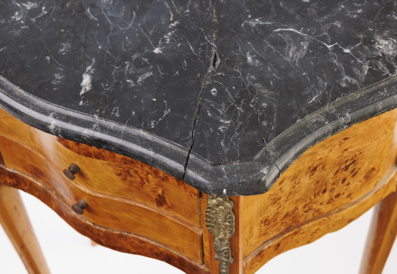 Corner of the black marble top showing the molded edge, natural white veining, and a stabilized crack, above a gilt-metal mount