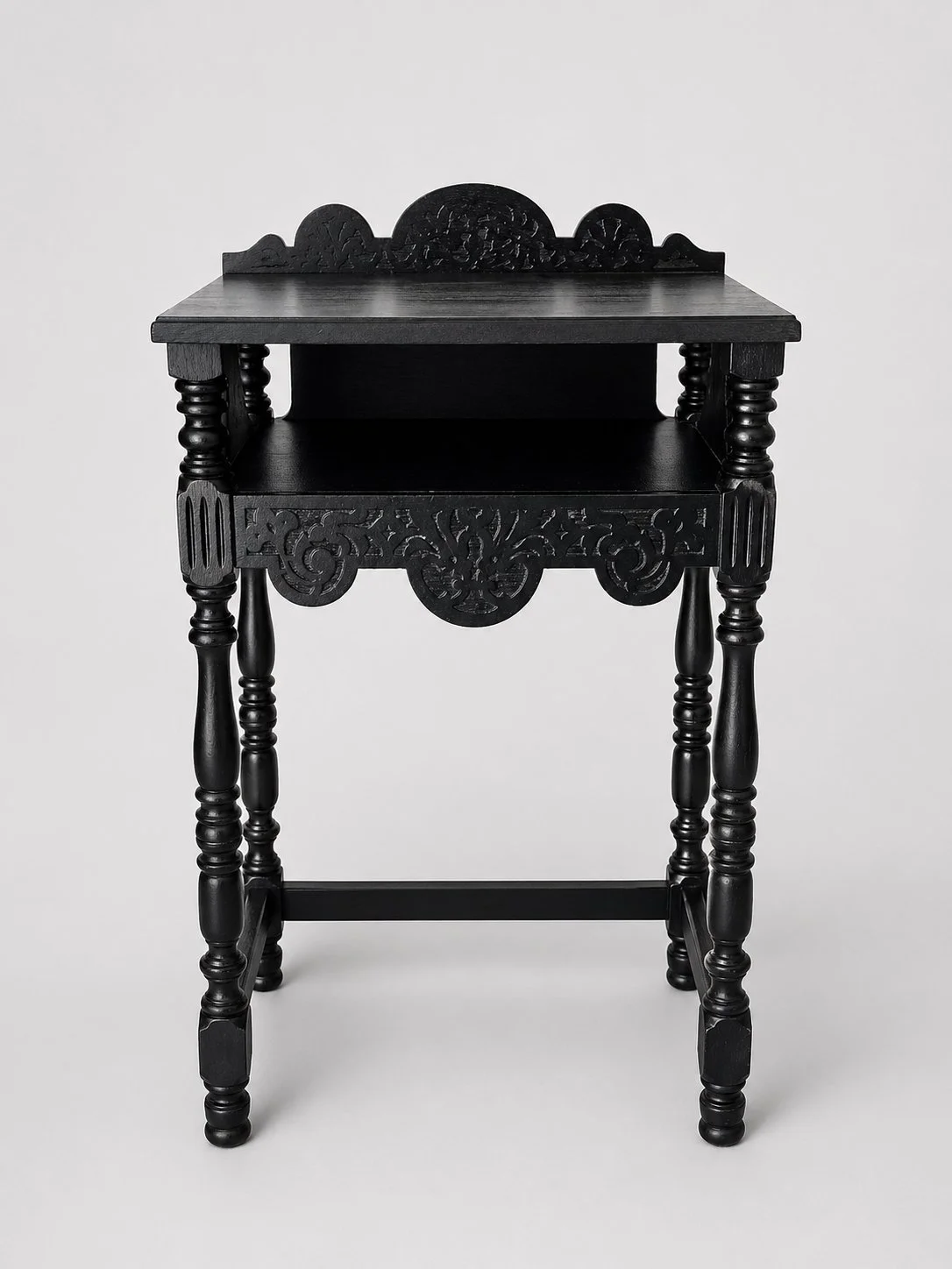 Front view of antique telephone stand with carved apron, lower shelf, and black stained finish emphasizing structure