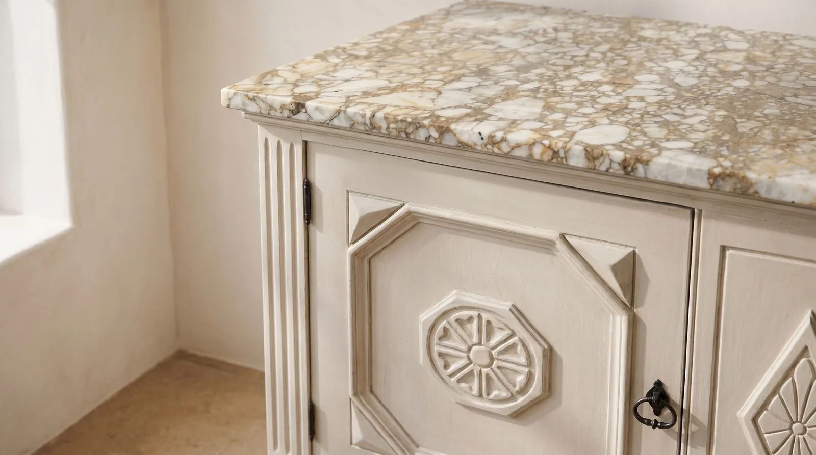 Close view of the cabinet's veined stone top and a carved door medallion in a sunlit room