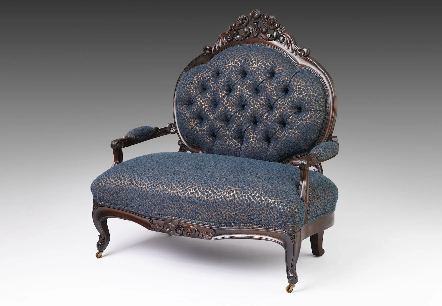 Antique Victorian Rococo Revival settee with a carved pierced rose crest, deep button-tufted medallion back, and cabriole front legs on brass casters, reupholstered in blue wool bouclé with copper glints