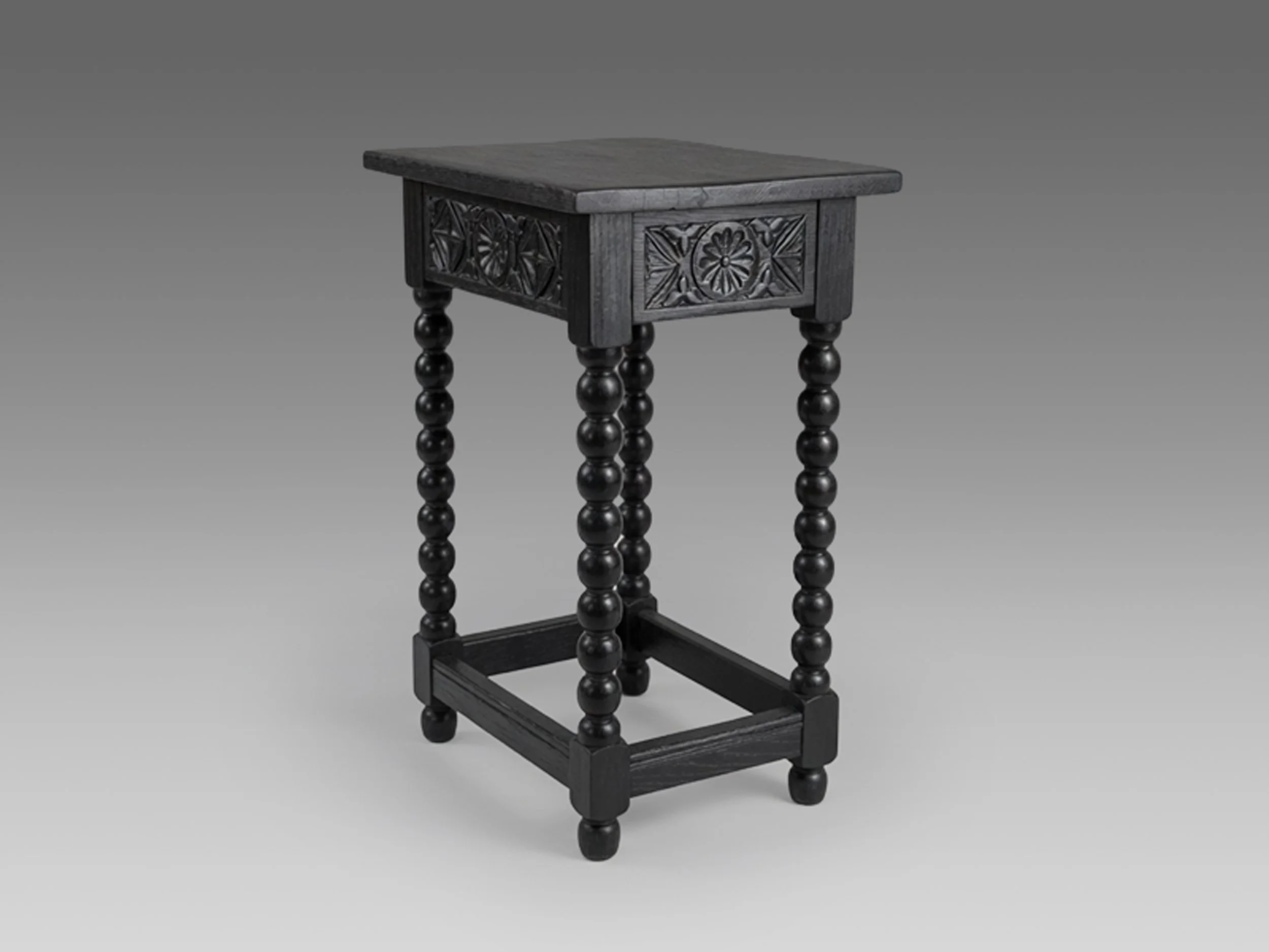 Spanish Revival flip top side table from the 1920s with carved geometric apron, turned legs, stretcher base, and black refinished wood surface.