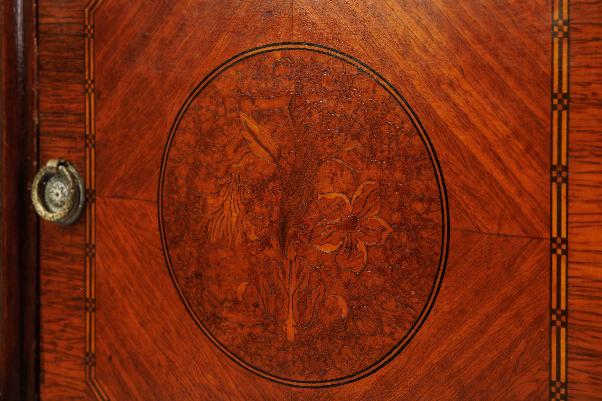 Floral marquetry door of The Carved Bloom, a flowering stem cut from contrasting veneers within an oval reserve, with a ring pull.